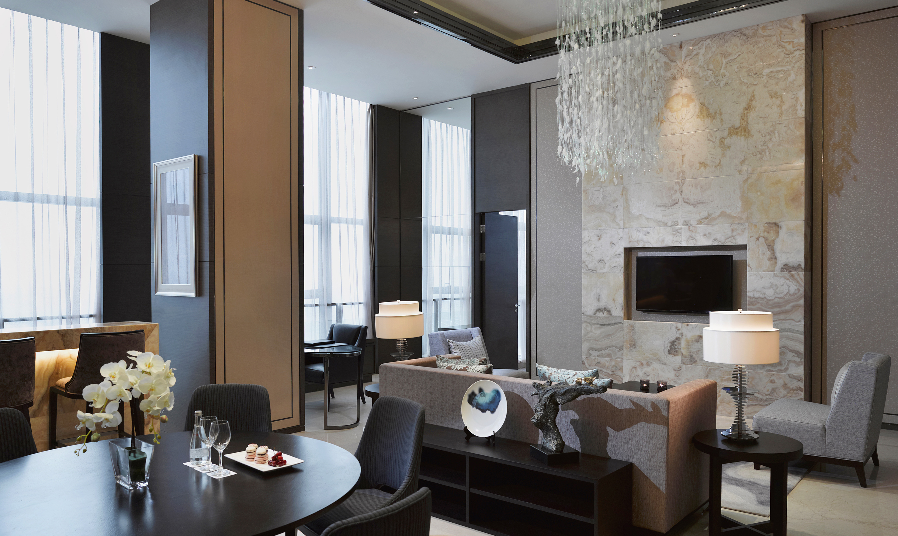 Luxury hotel suite with modern living and dining areas, chandelier.