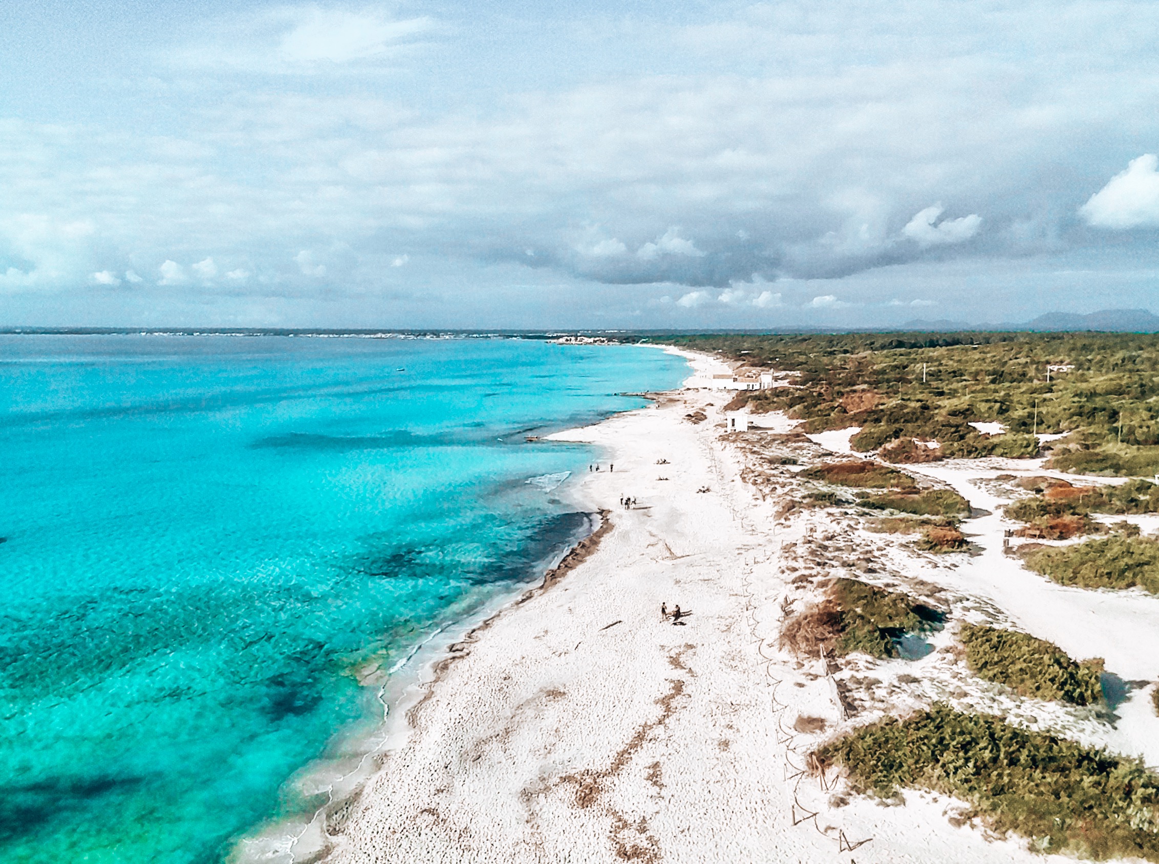 Vista aérea: playa de arena blanca, mar turquesa y dunas verdes.