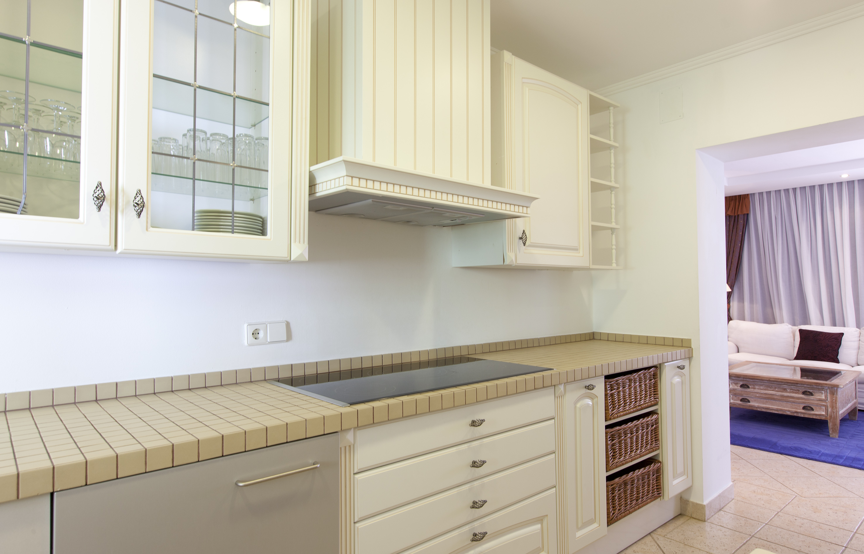 Modern kitchen with white cabinets, tiled countertop, built-in hob, open living.