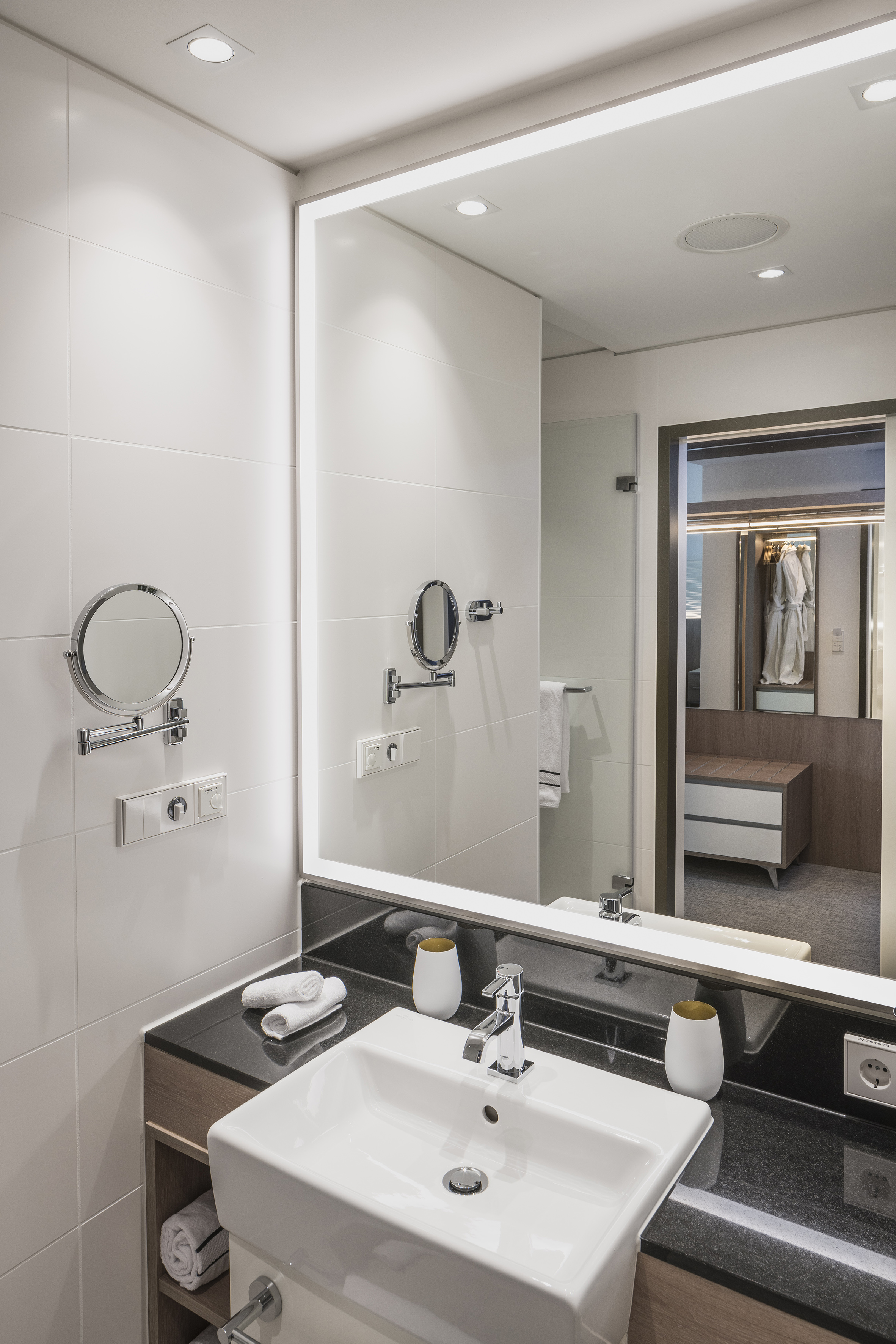 Bright modern bathroom vanity: LED mirror, white sink, black counter.