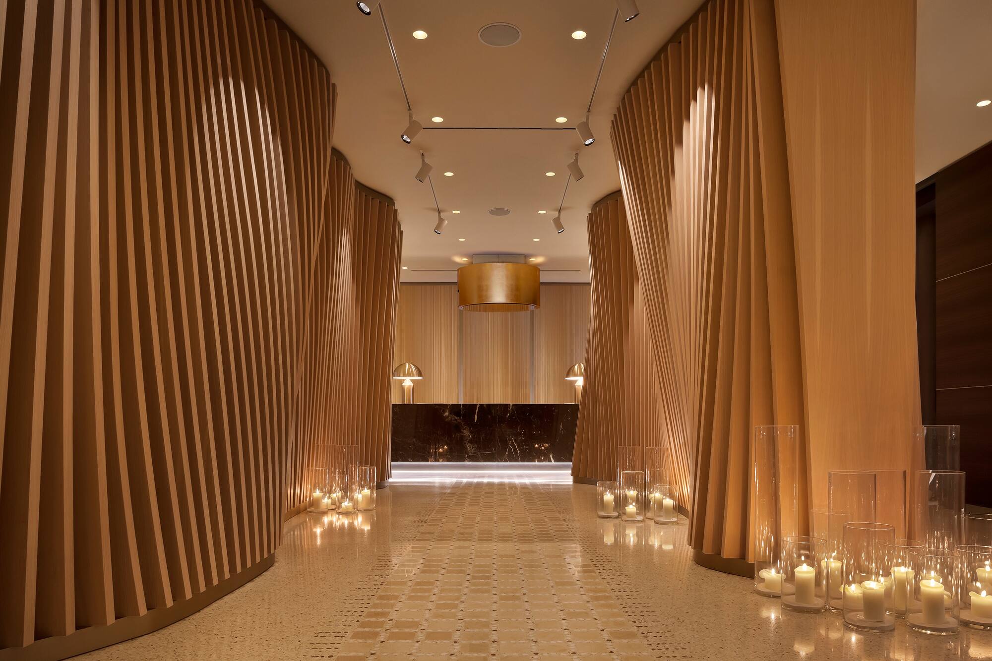 Contemporary hotel lobby, curved wood paneling, warm candles, marble desk.