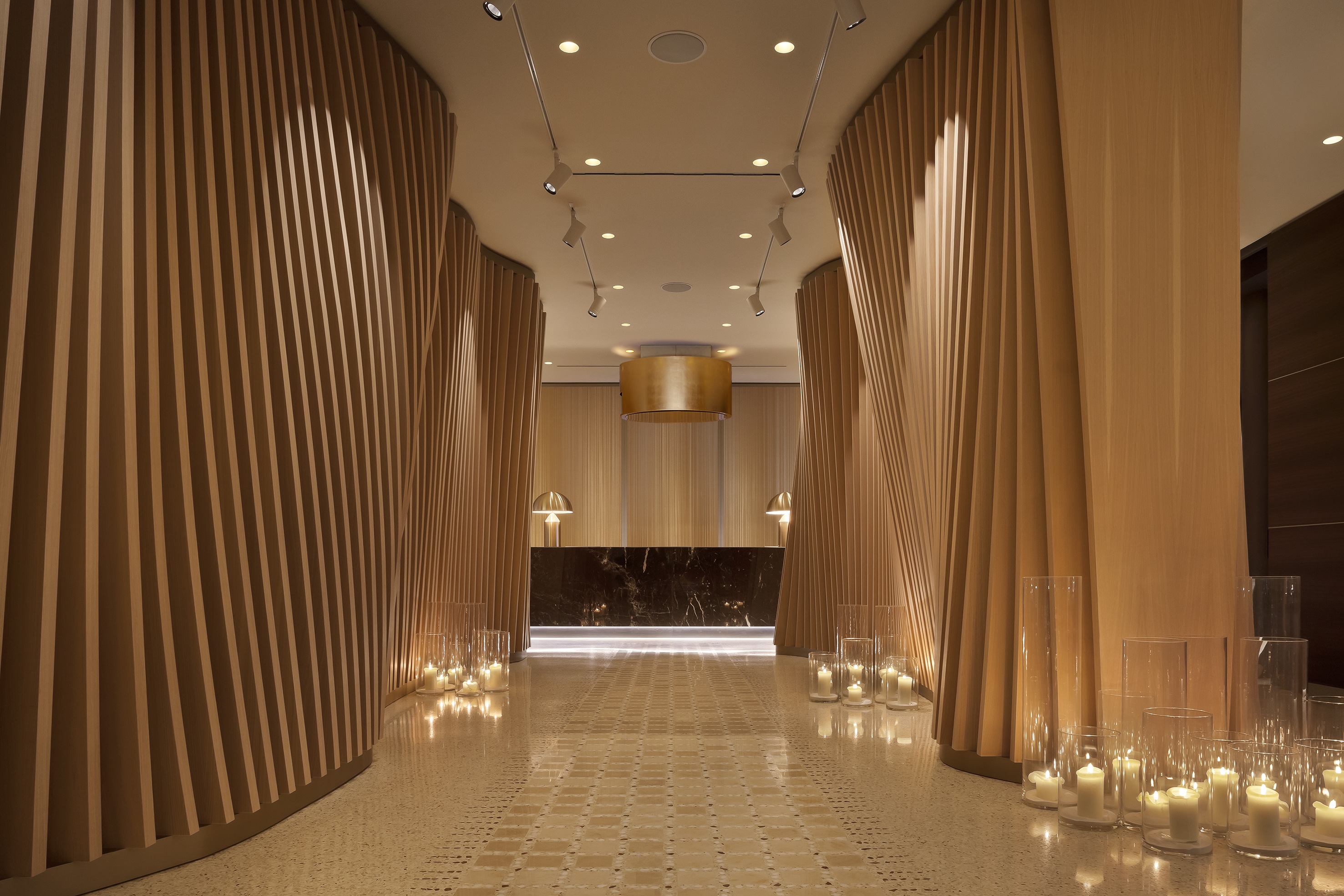 Contemporary hotel lobby, curved wood paneling, warm candles, marble desk.