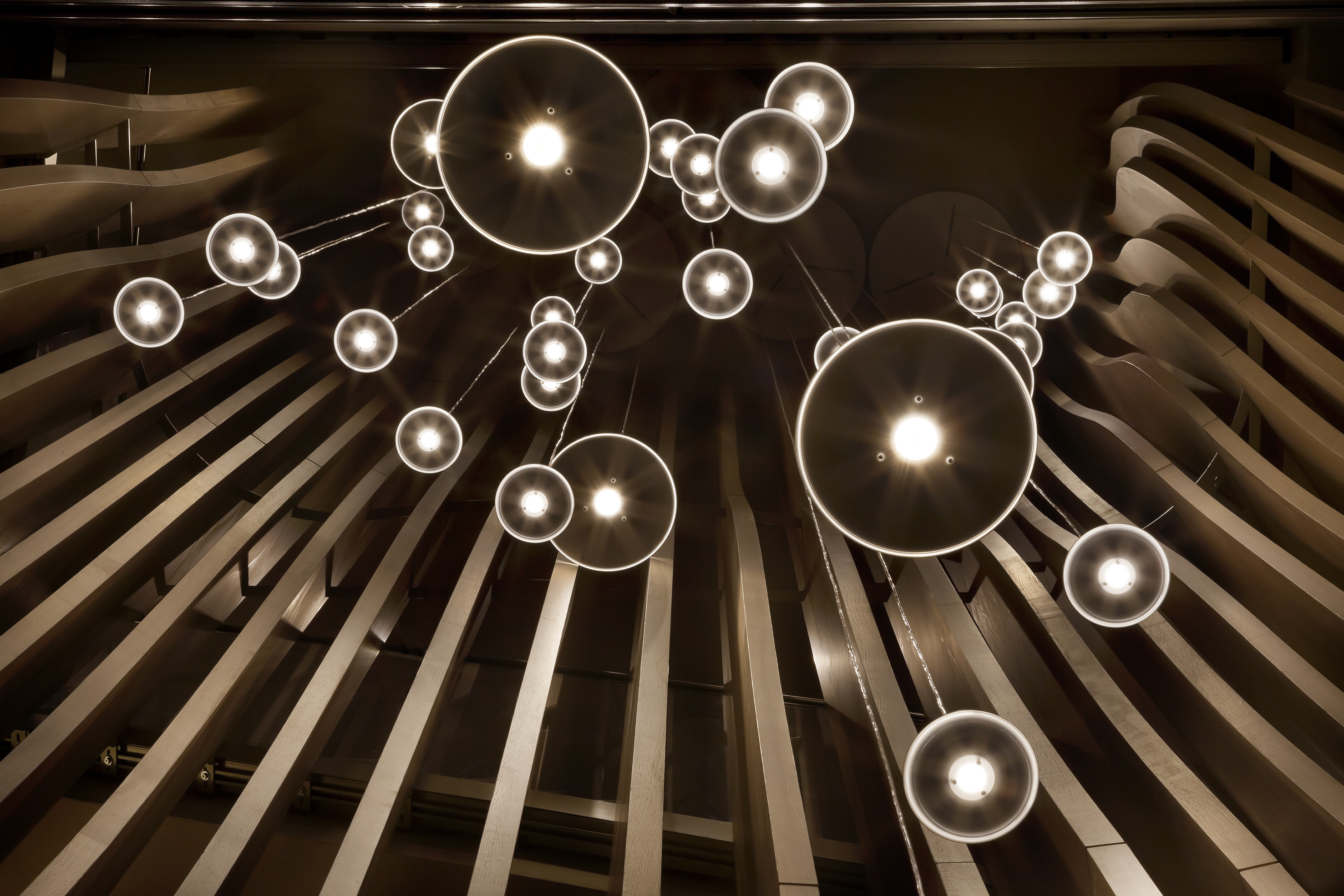 Modern glowing pendant lights against a dark, sculptural architectural ceiling.