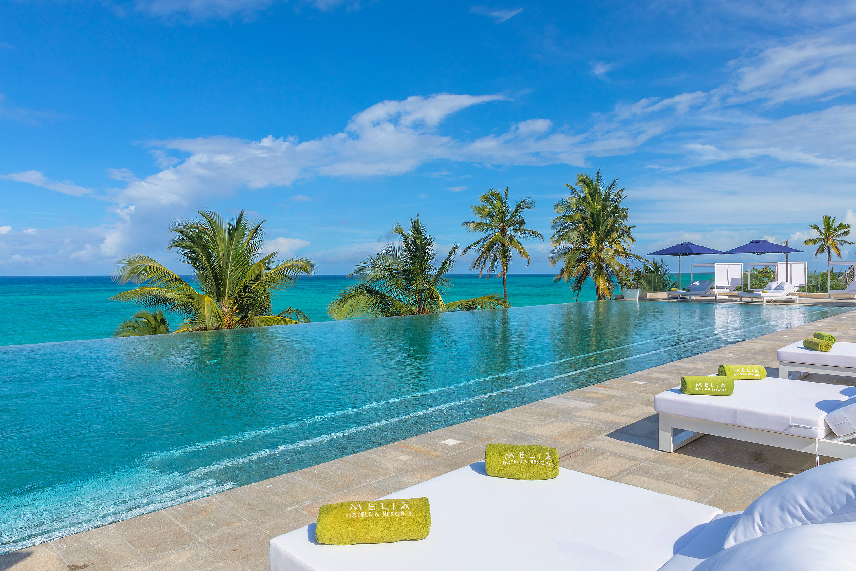 Melia resort infinity pool, turquoise ocean, palm trees, white lounge chairs.