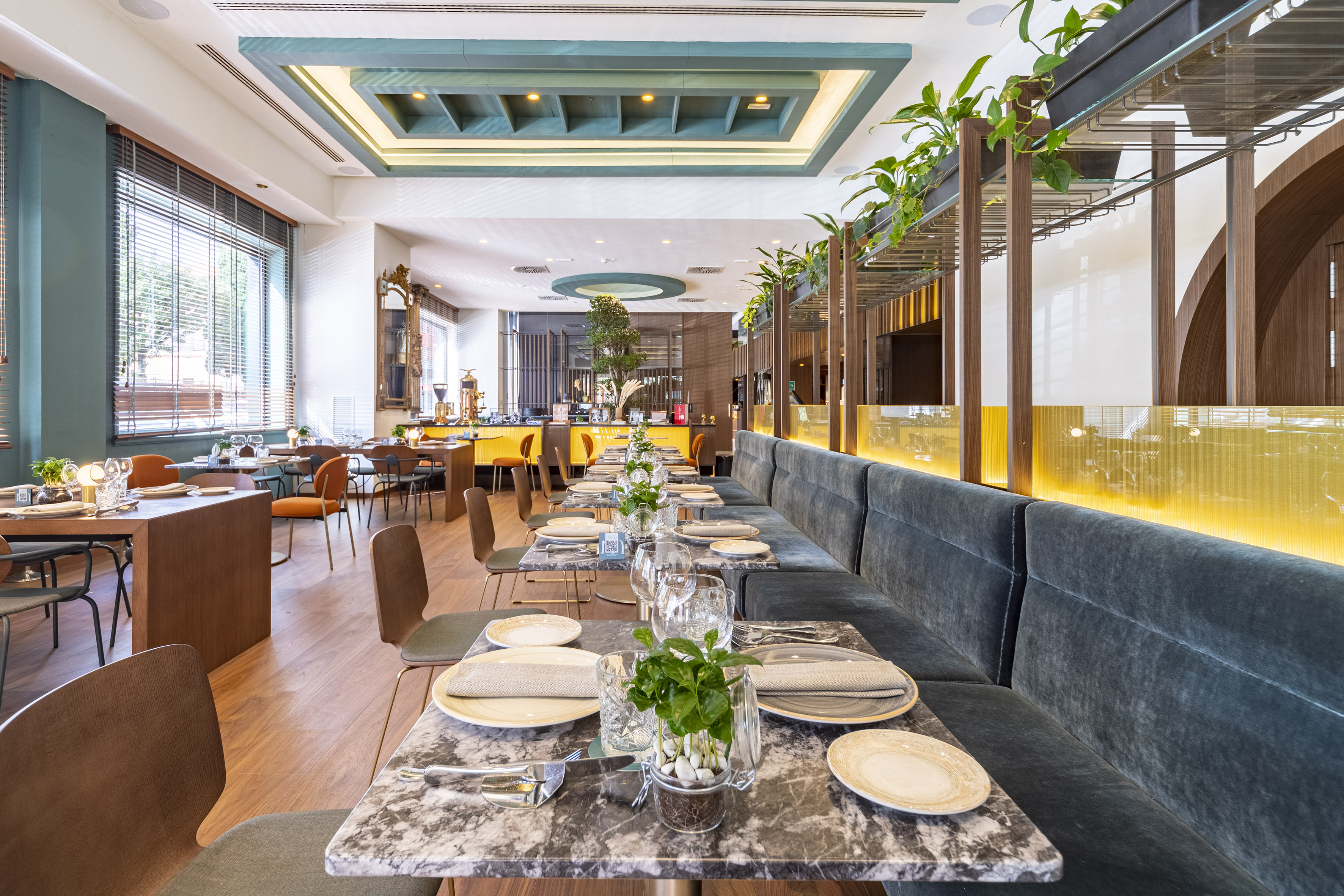Modern hotel restaurant with velvet seating, marble tables, and green plants.
