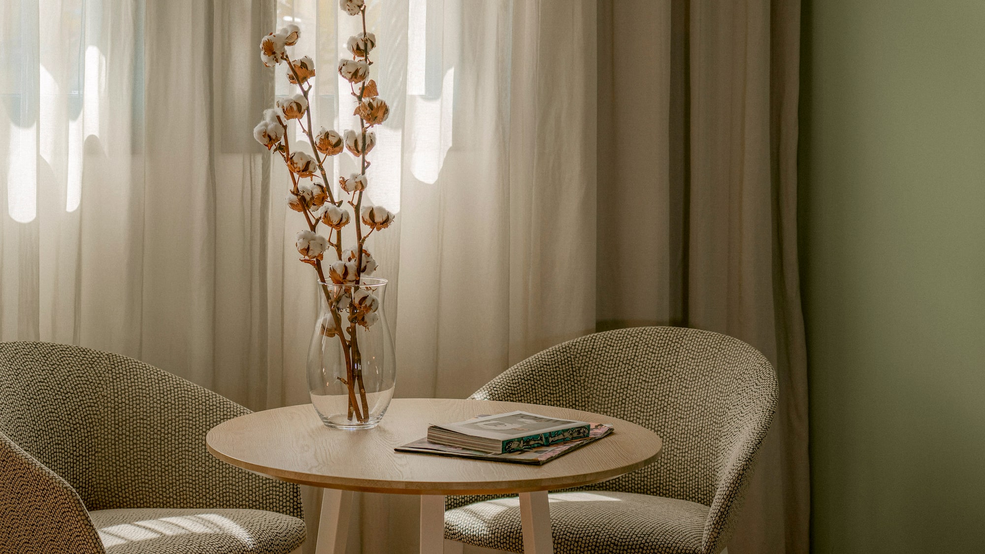 a table with a vase of cotton flowers and a book
