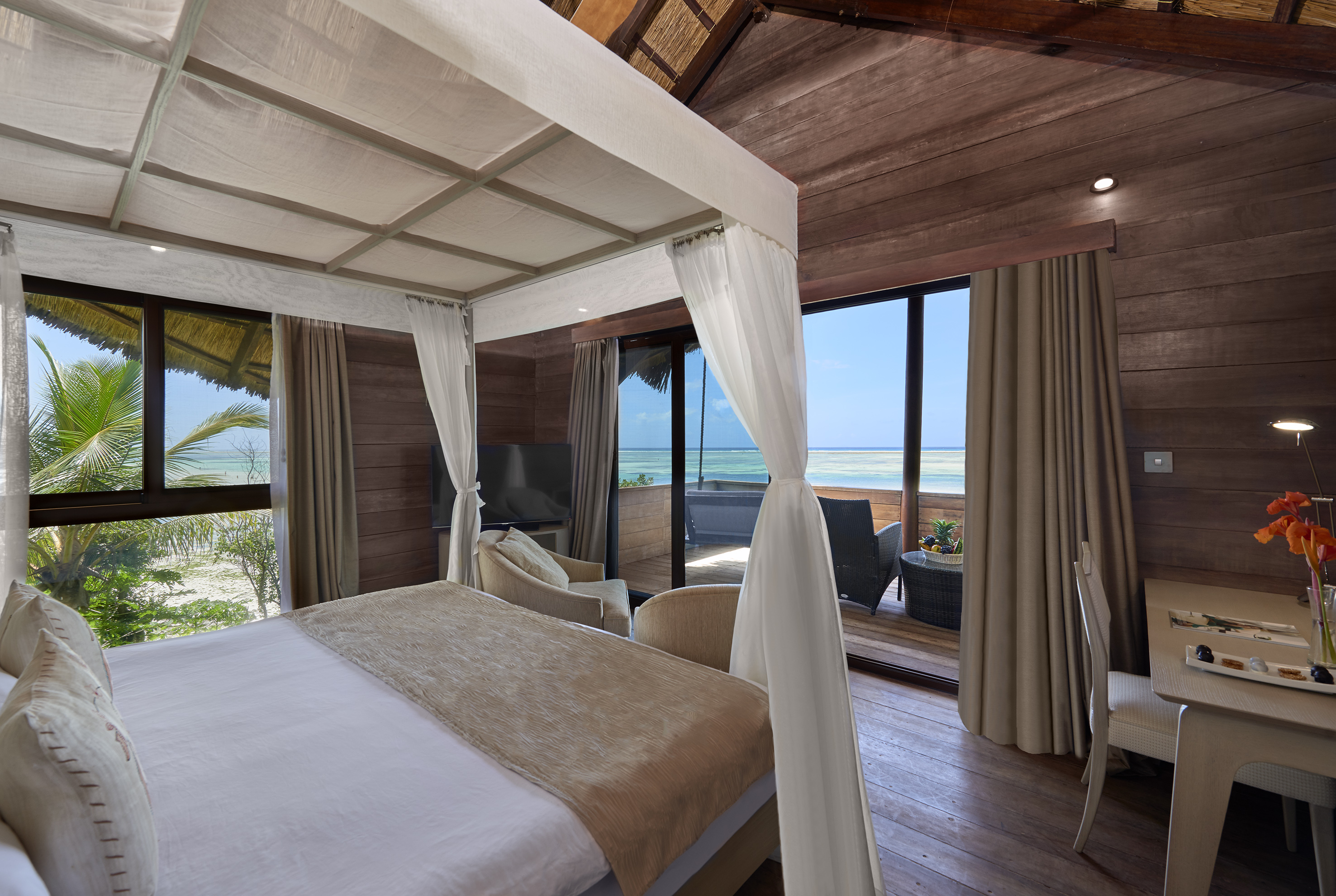 Luxury tropical bedroom with four-poster bed, ocean and beach views.