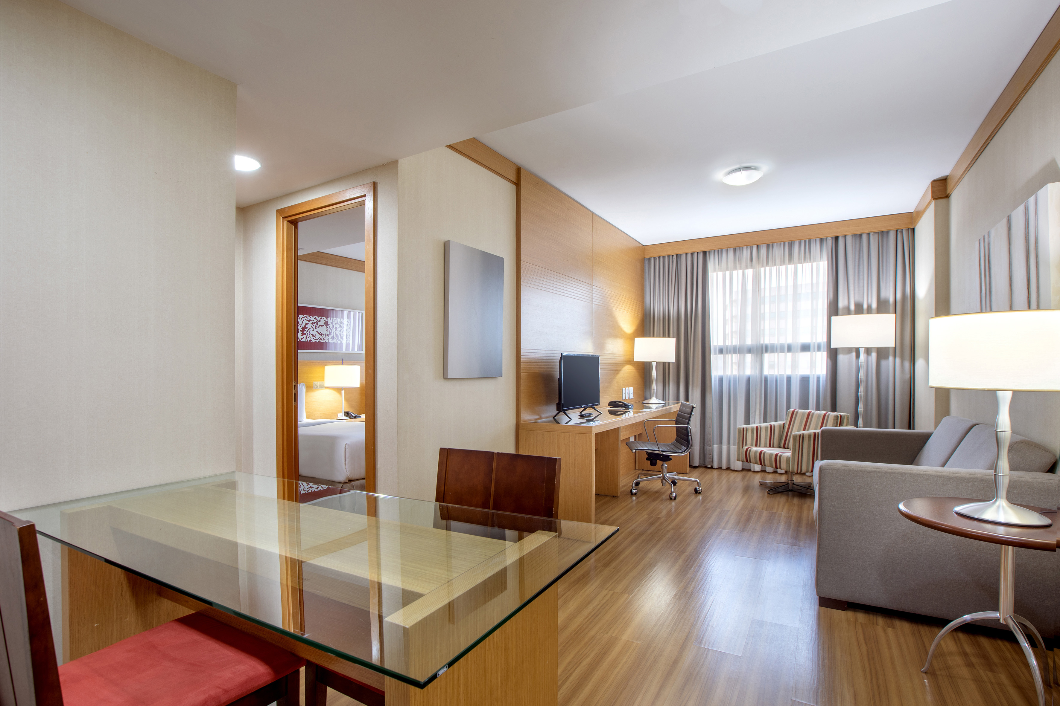 Modern hotel suite living room with dining area, desk, and open bedroom.