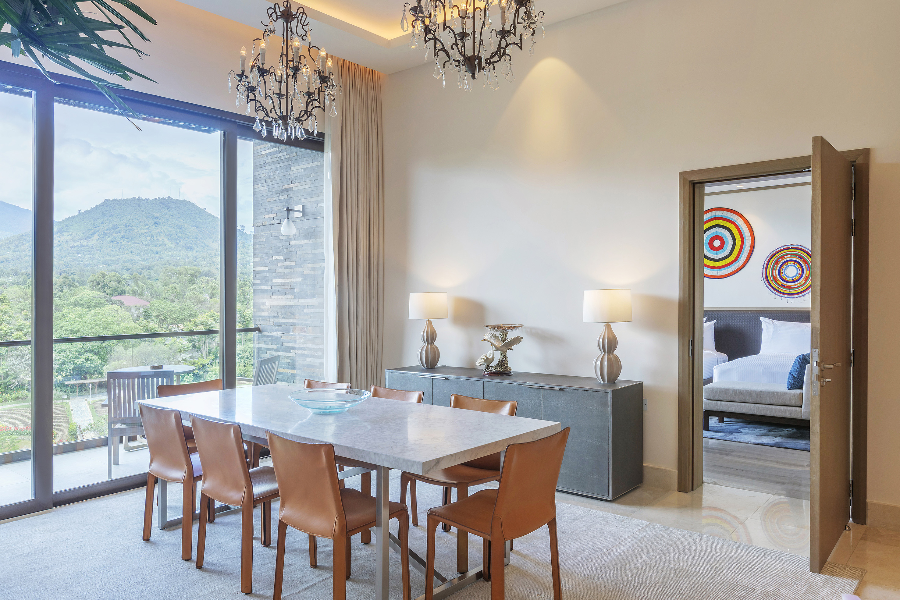 Modern dining room with mountain view, marble table, leather chairs, and chandeliers.