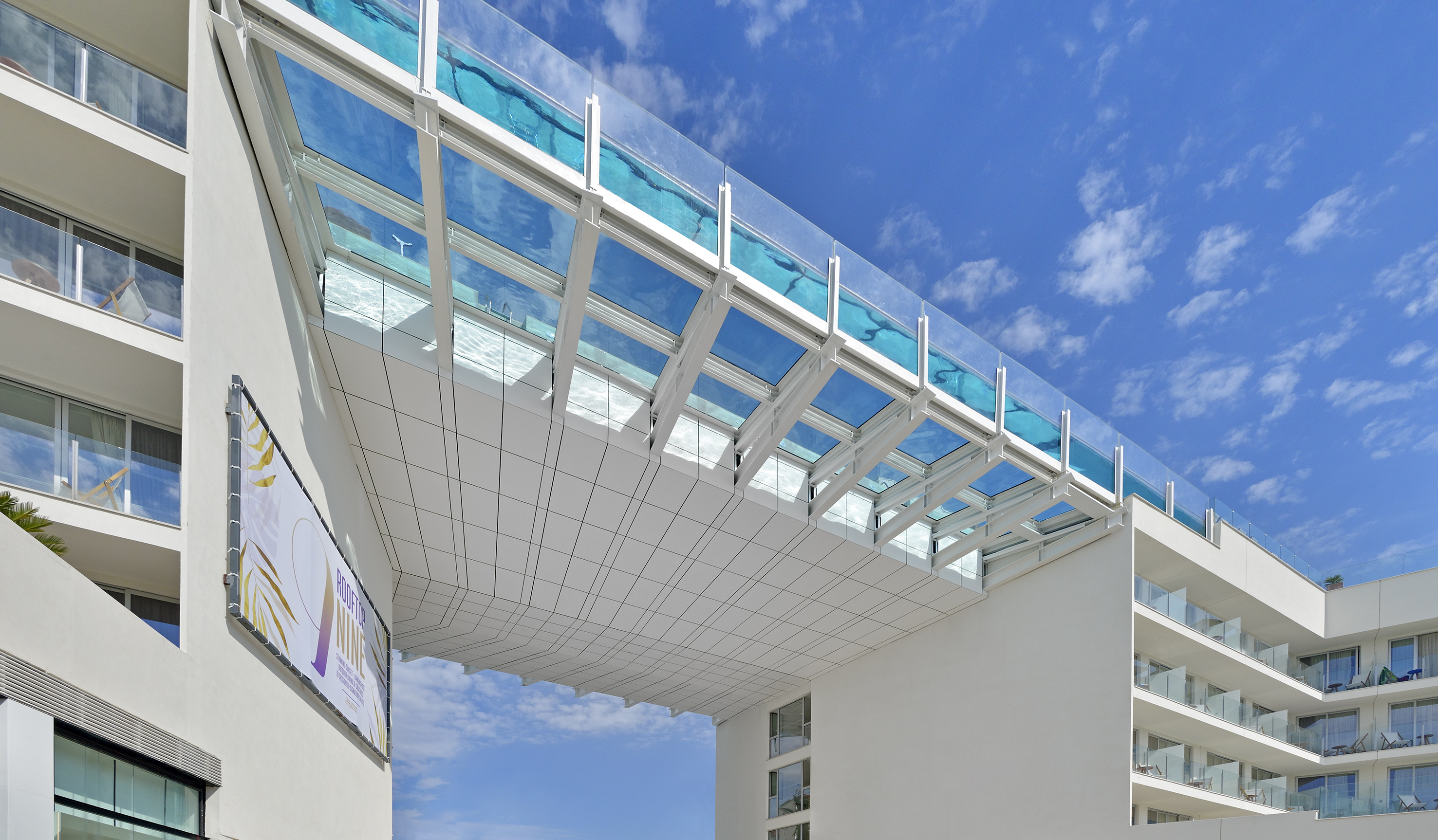 Modern hotel building with elevated transparent glass pool bridge.