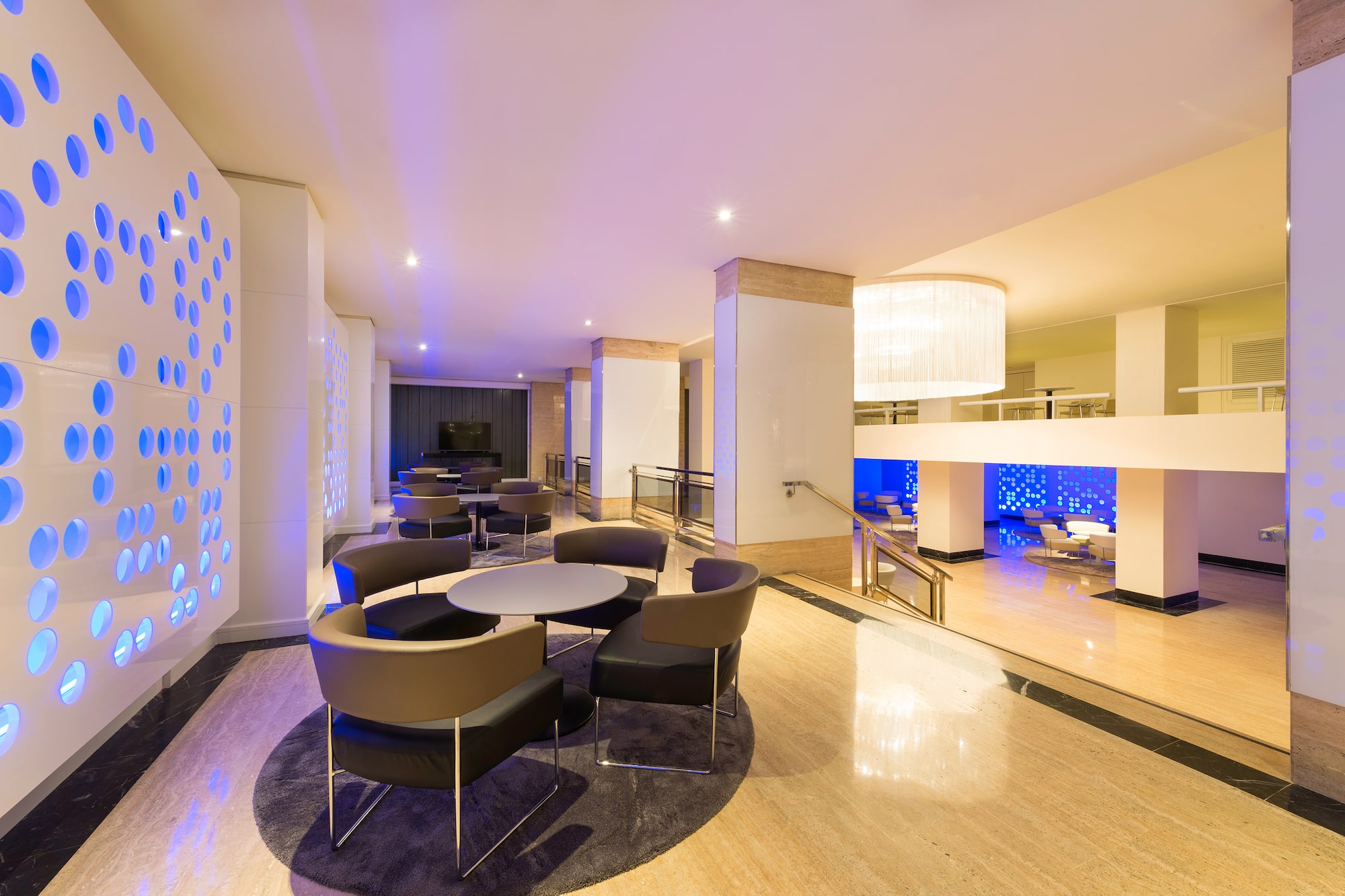 Contemporary hotel lounge with blue-lit wall, modern chairs, and marble floor.