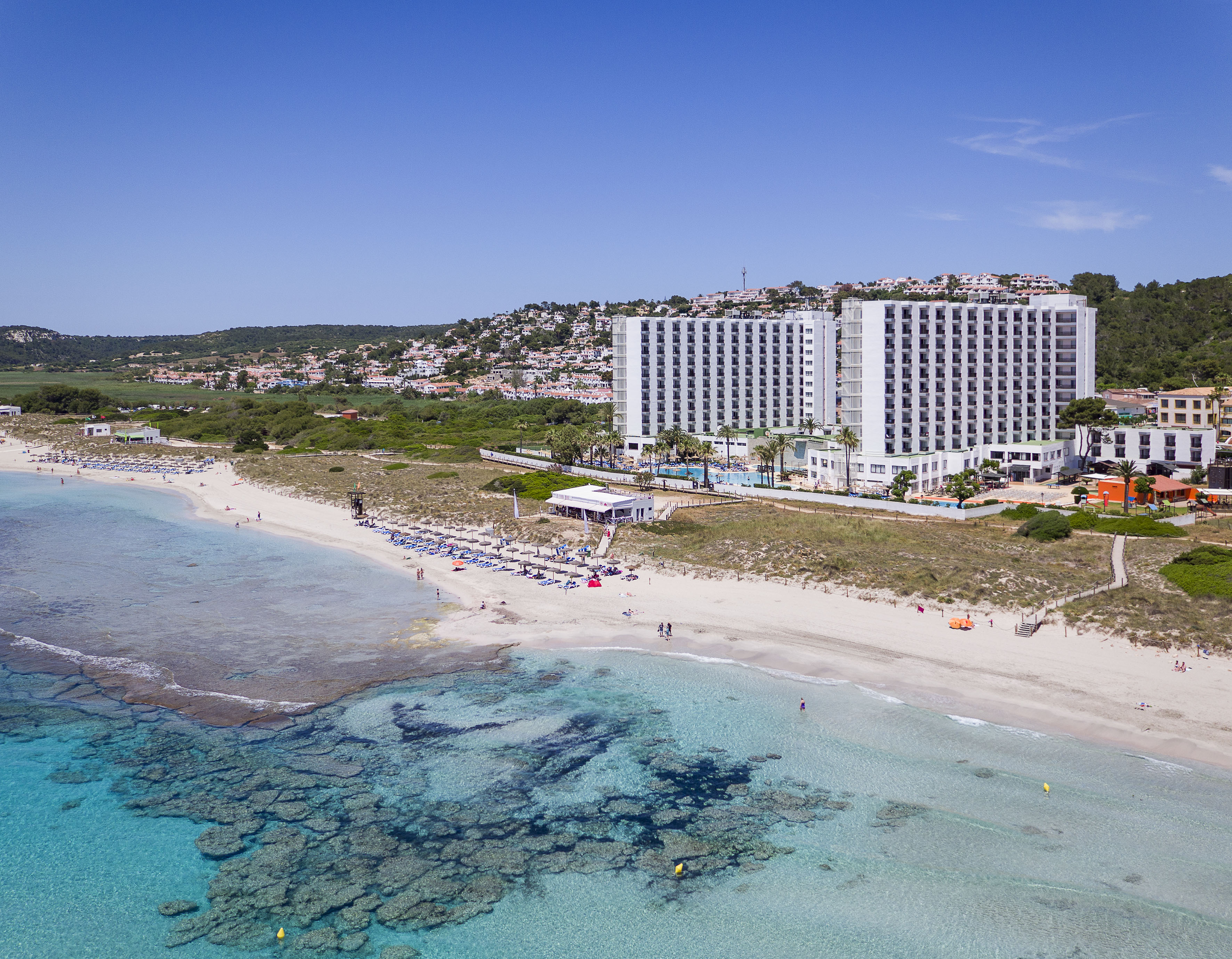 Beach resort aerial: White sand, clear turquoise water, and large hotel complex.