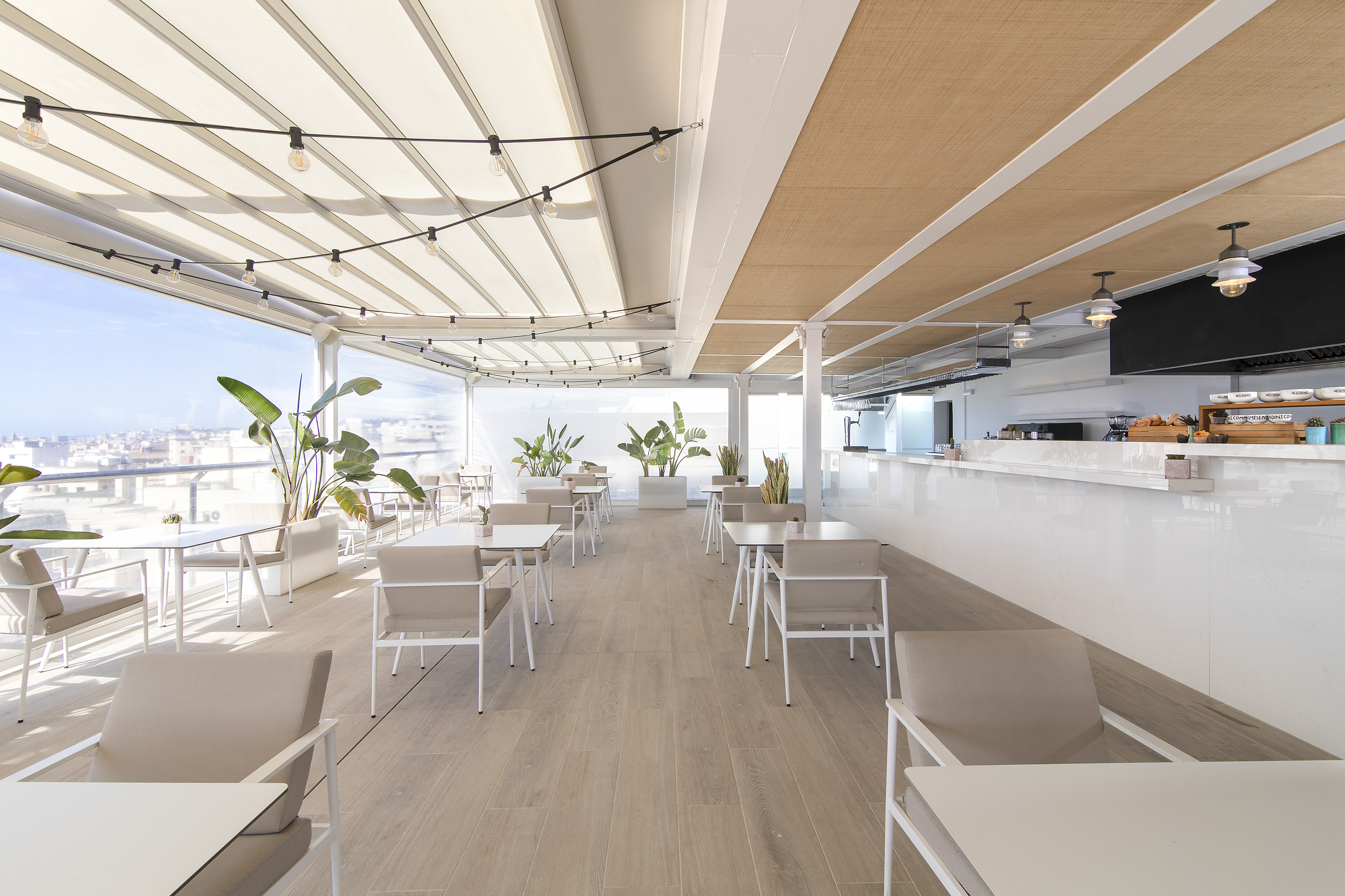 Rooftop restaurant terrace, outdoor seating, white furniture, plants, city view.