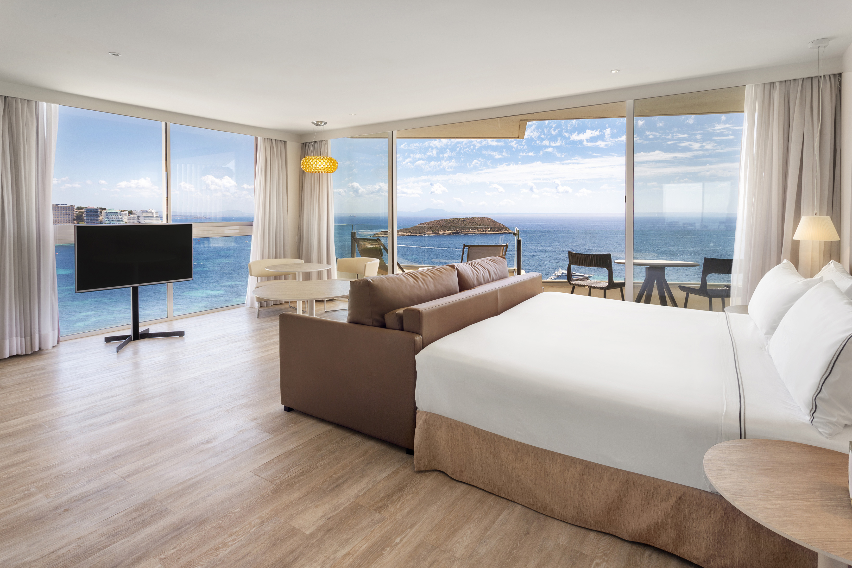 Modern hotel suite with panoramic ocean view, bed, sofa, and balcony.
