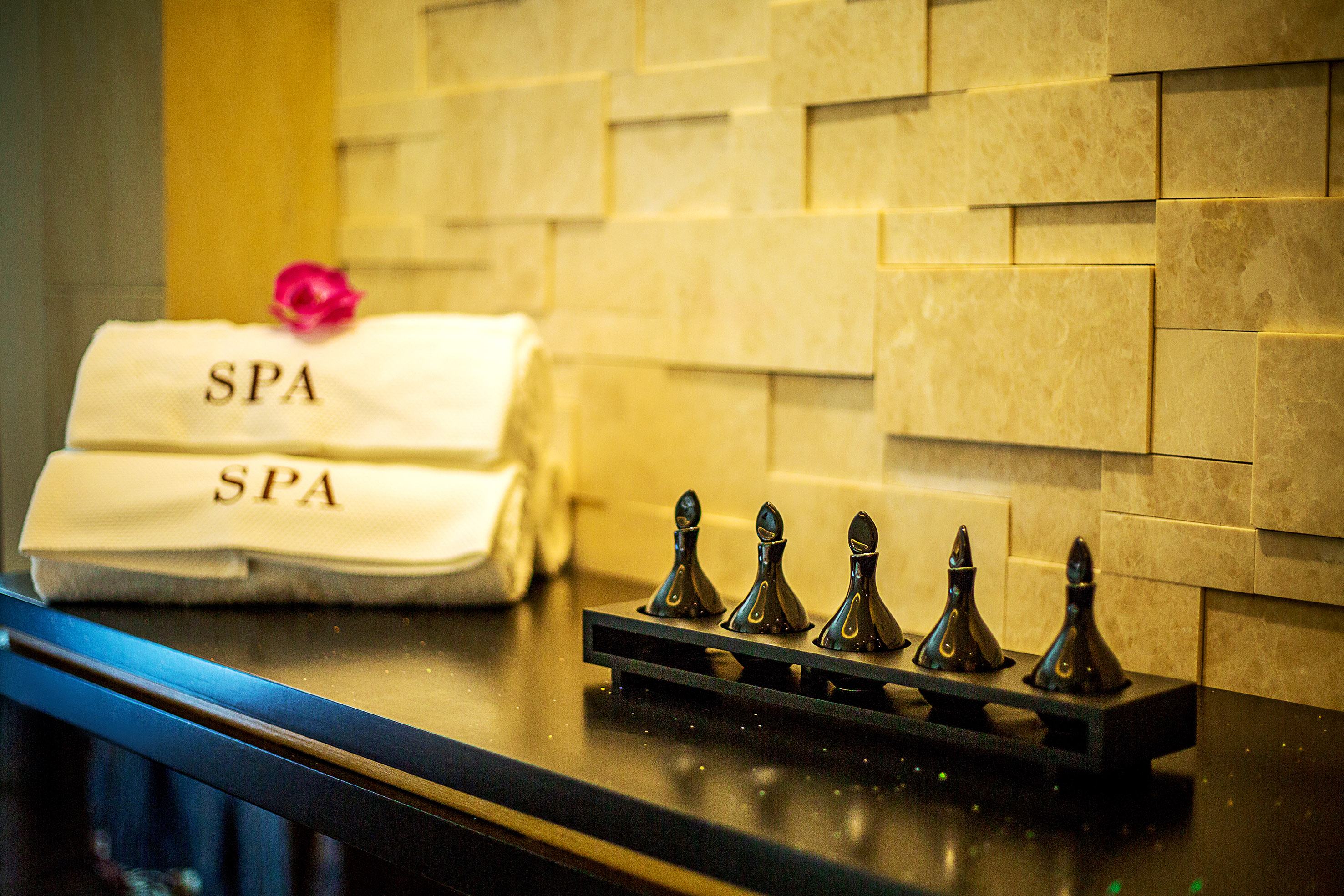White SPA towels, pink flower, and essential oil bottles on a dark spa counter.