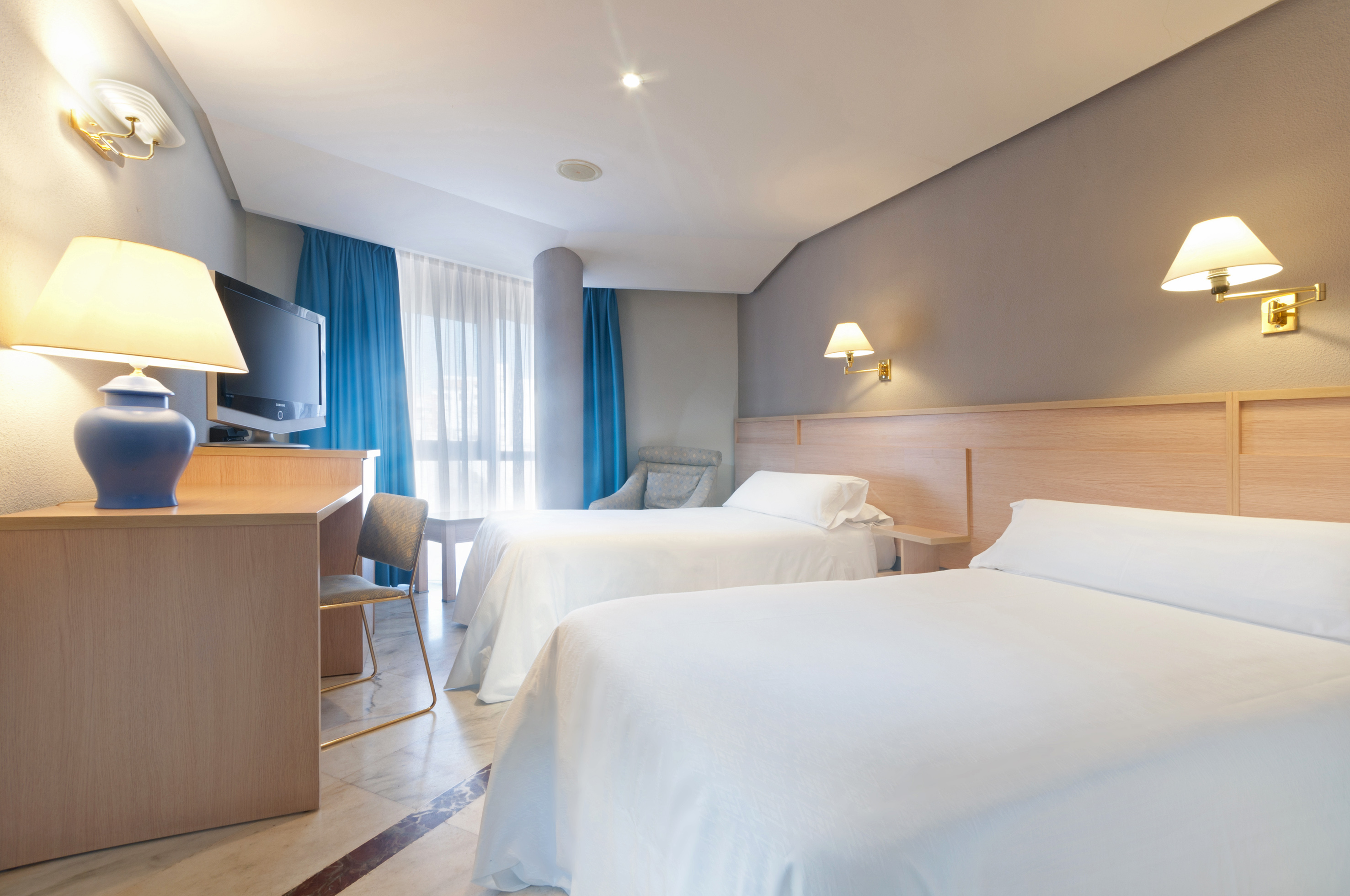 Hotel twin room featuring two beds, desk, TV, and blue curtains.