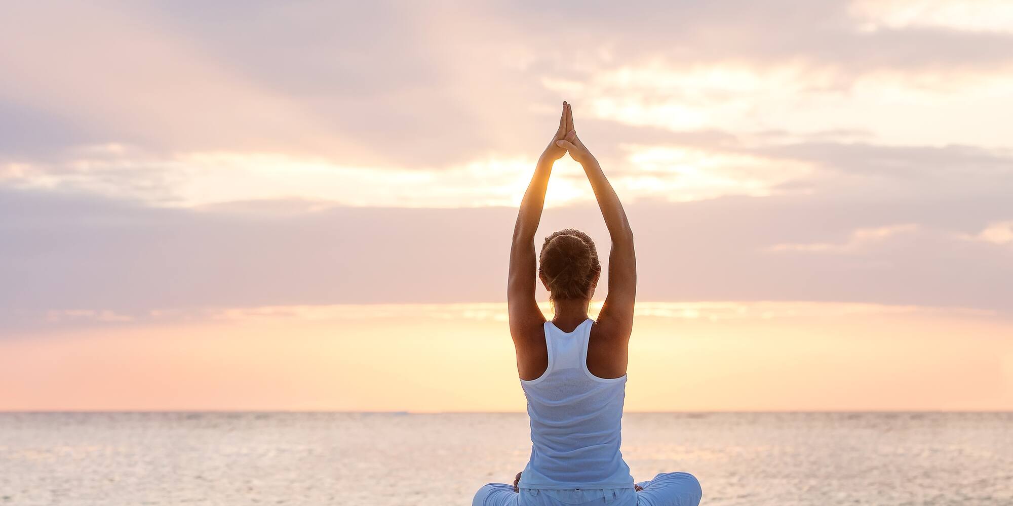 a woman sitting on the beach with her hands up