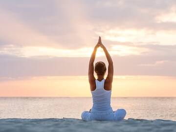 a woman sitting on the beach with her hands up