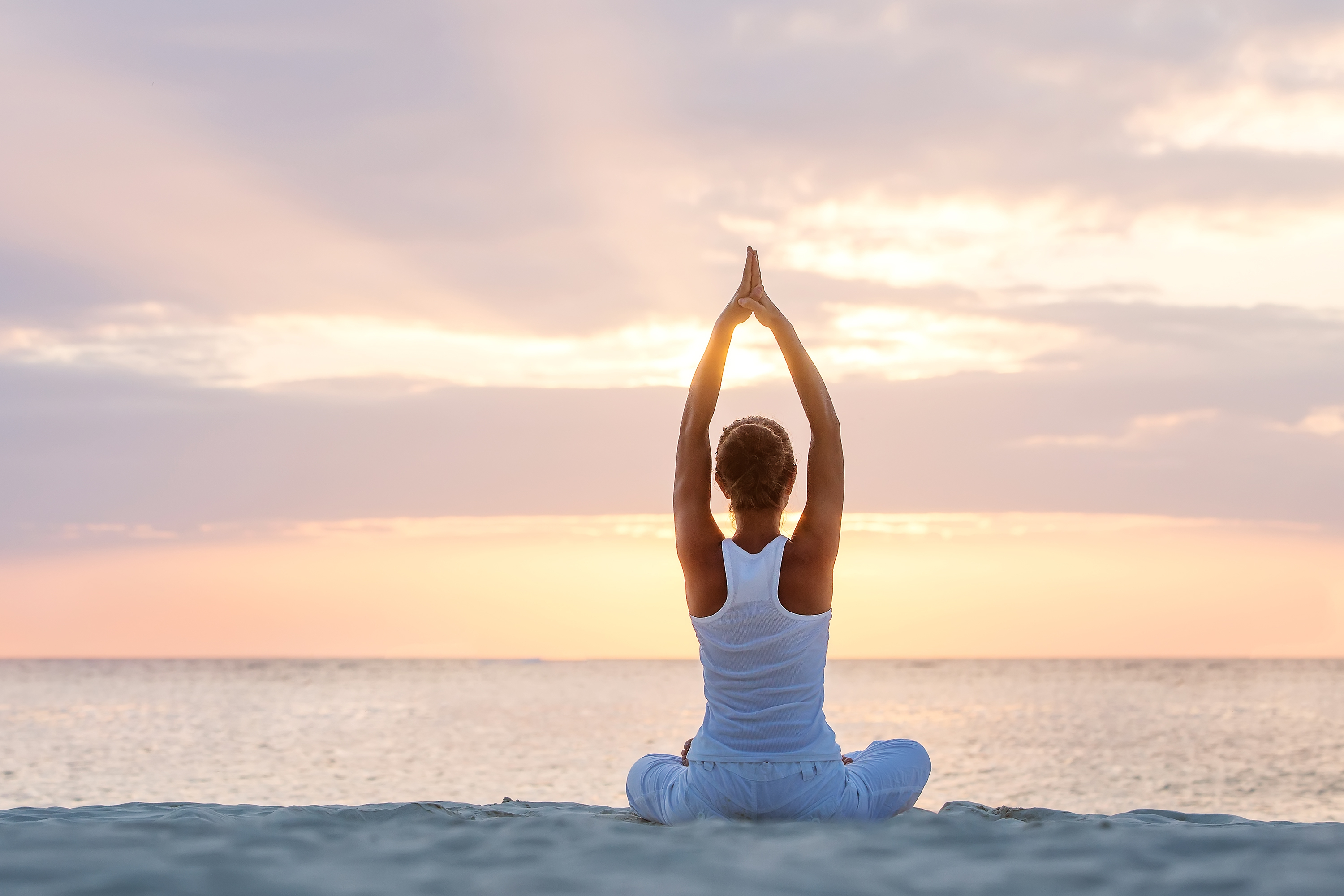 Woman doing yoga meditation on sandy beach at sunset.