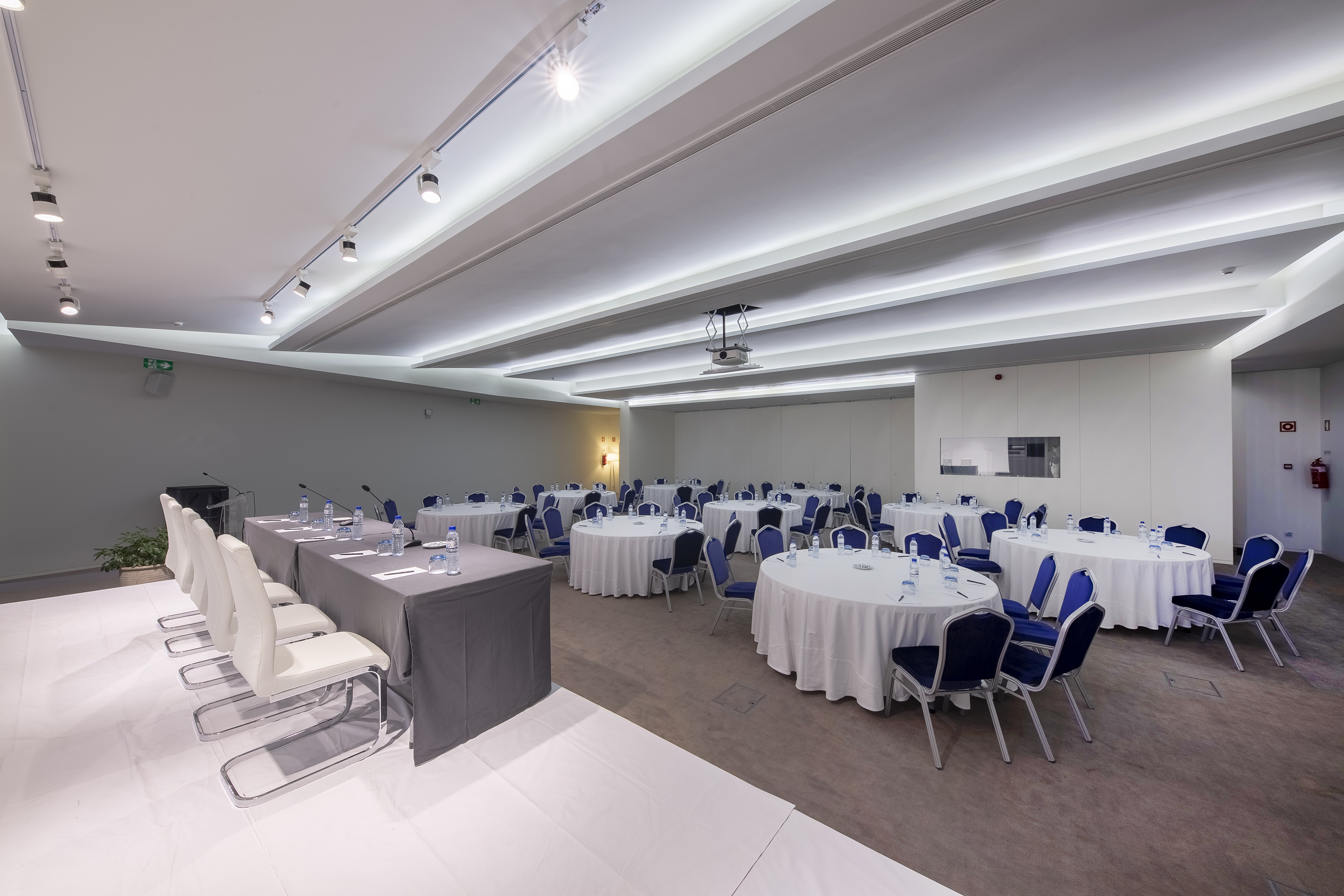 Spacious meeting room with round tables, blue chairs, and presentation setup. - Auditórium Mafalala - Meliá Maputo Sky, Maputo