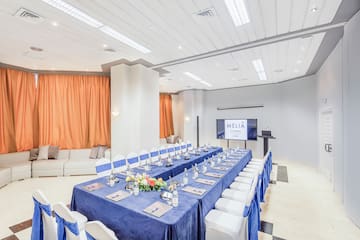 a long table with blue tablecloths and chairs in a room with a television