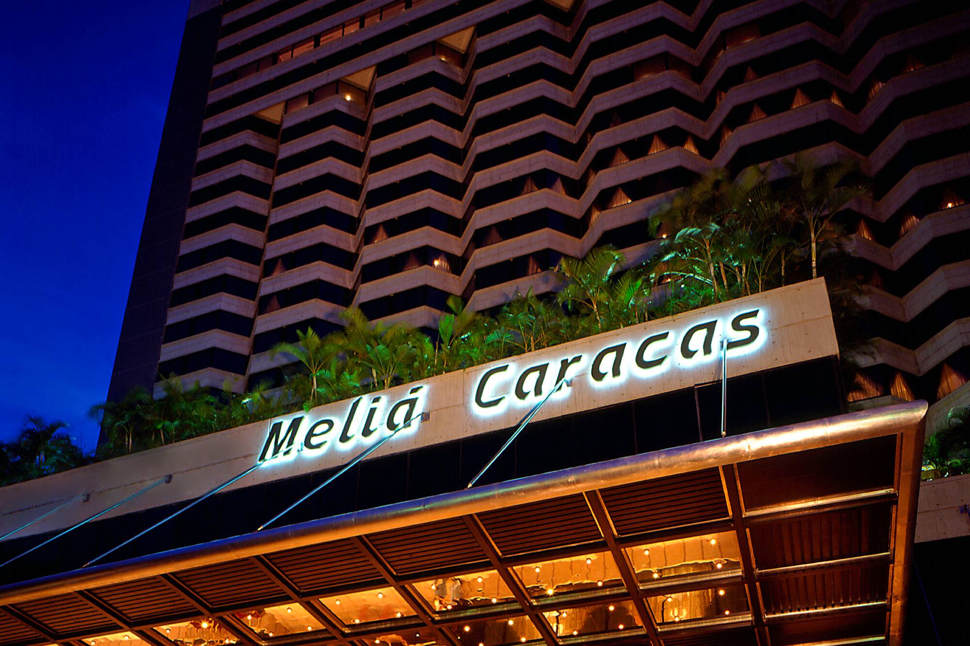 Illuminated Melia Caracas hotel exterior at dusk with a black limousine.