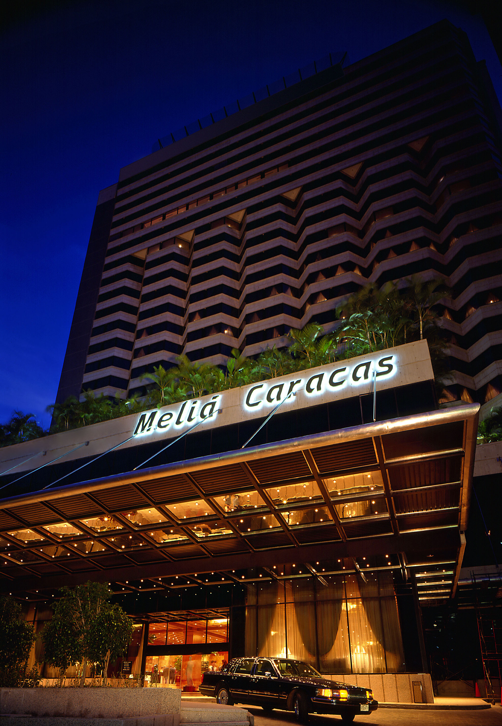 Illuminated Melia Caracas hotel exterior at dusk with a black limousine.