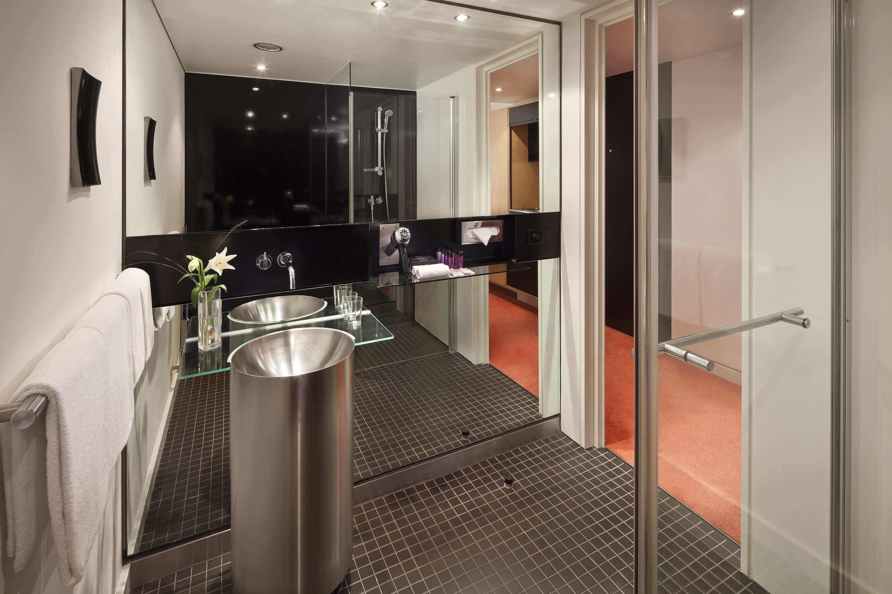 Sleek modern hotel bathroom with double sinks, large mirror, and glass shower.