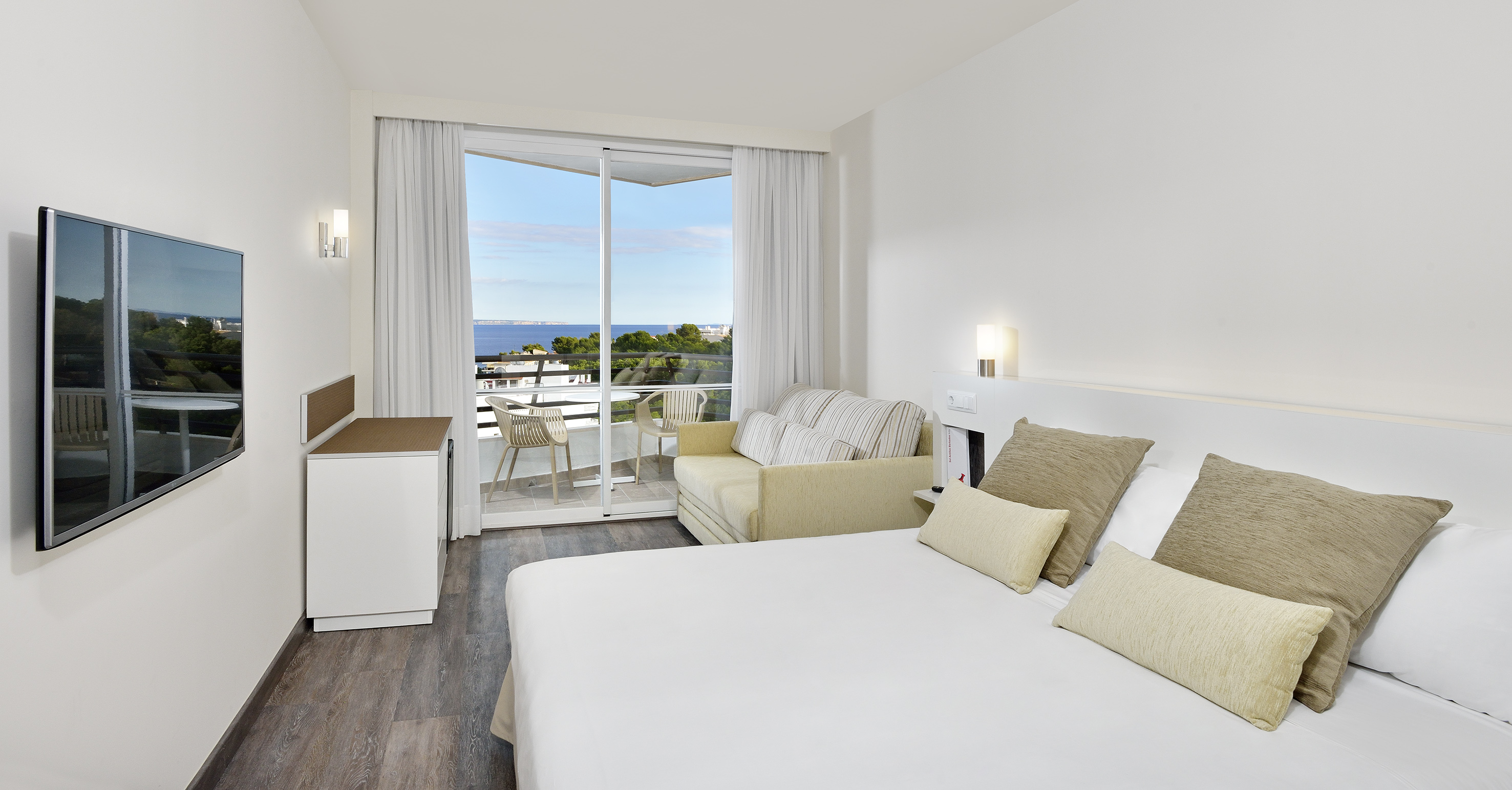 Modern hotel room with sea view, balcony, bed, and sofa.