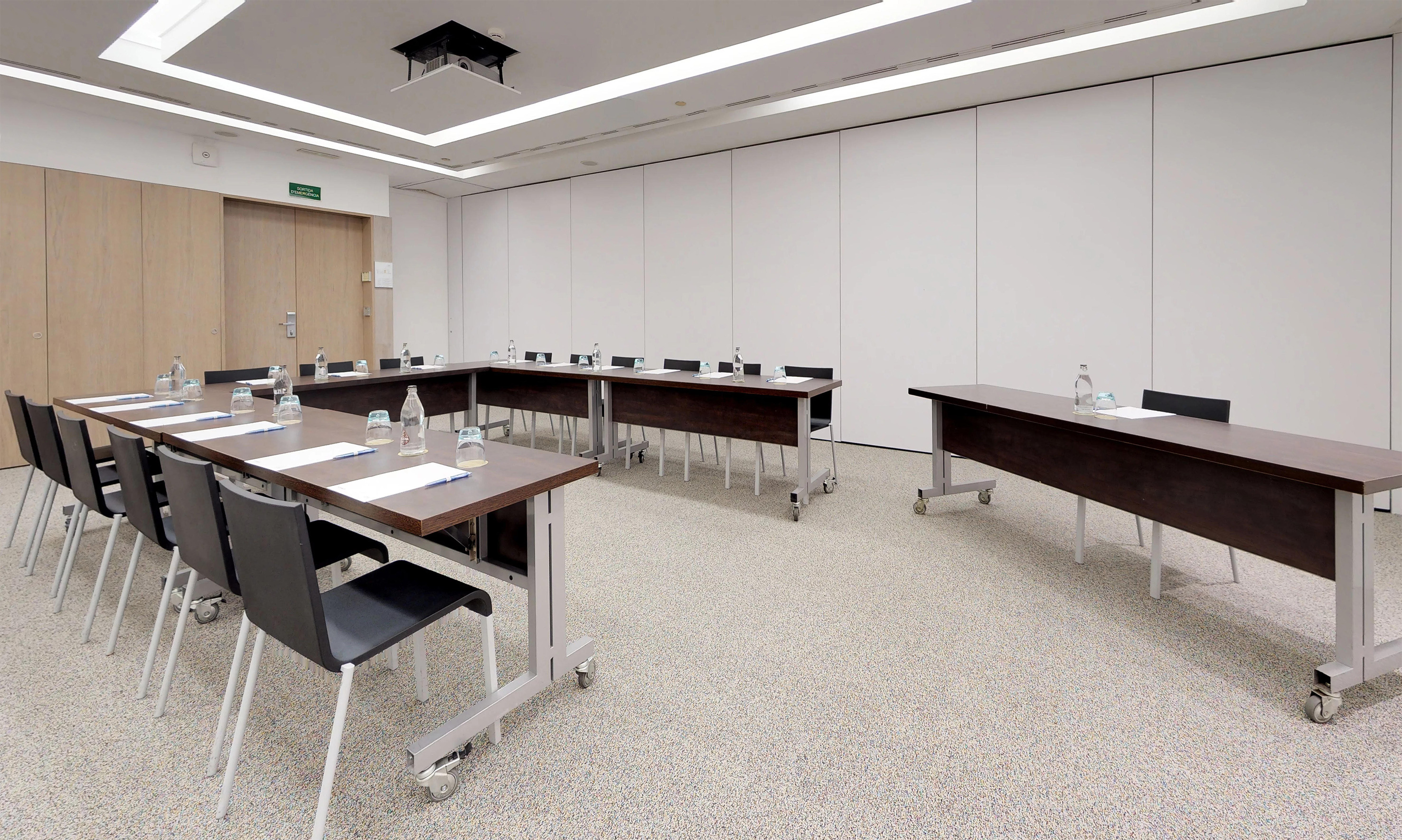 Modern conference room with U-shaped tables, black chairs, and projector.