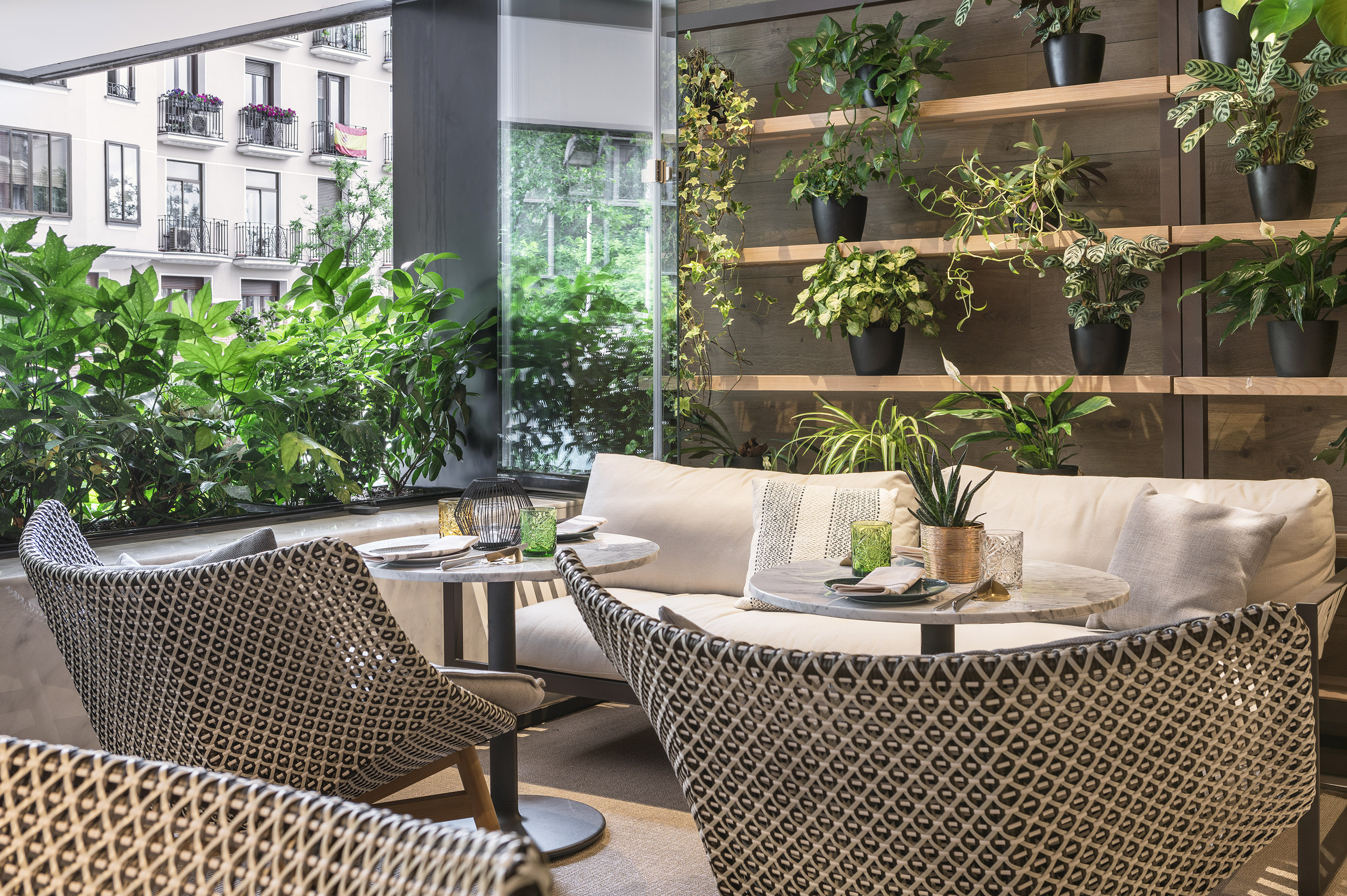 Modern cafe terrace with comfortable seating, marble tables, and lush plants.