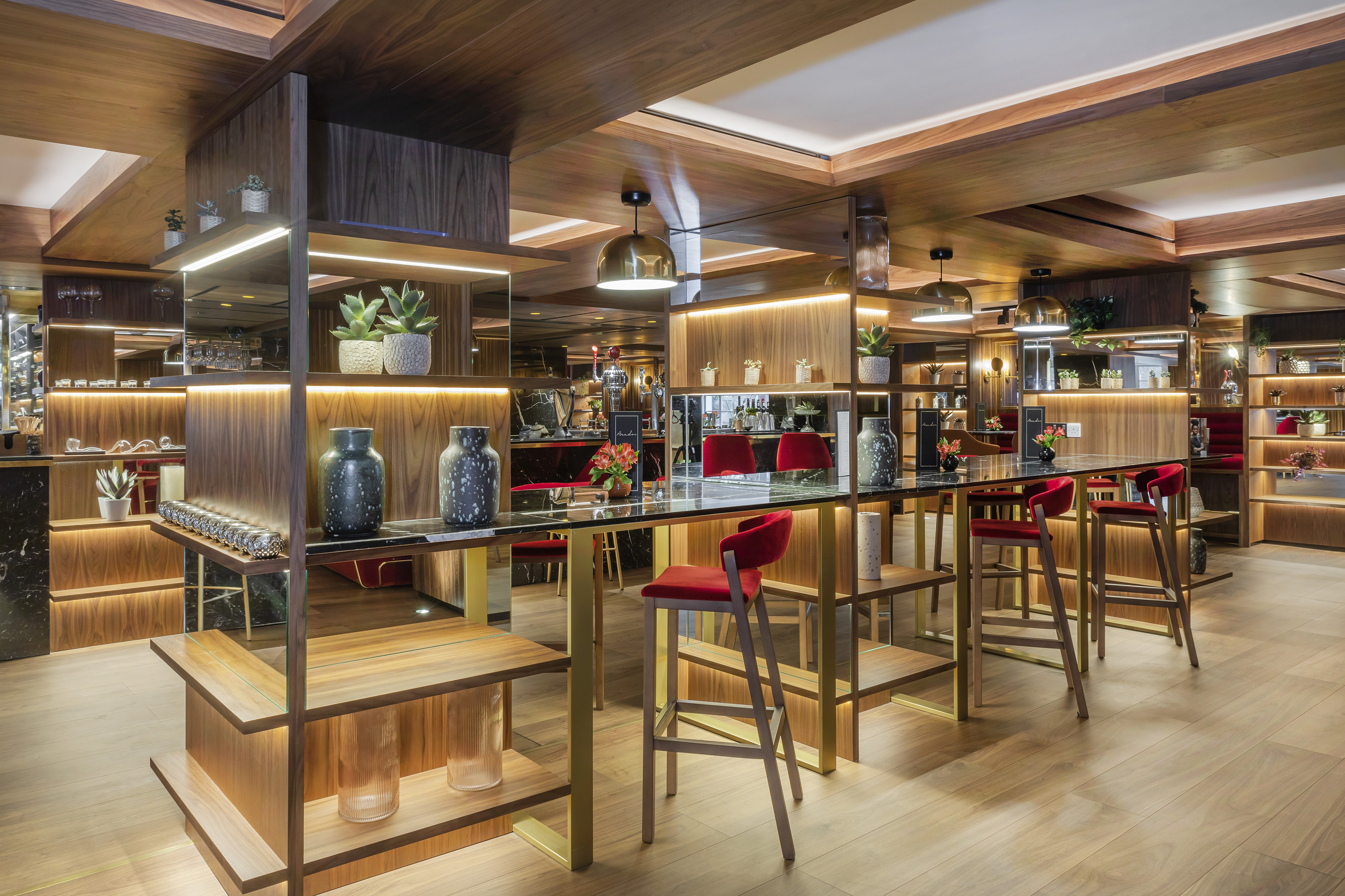 Modern elegant bar with red stools, illuminated wood shelves, and stylish decor.