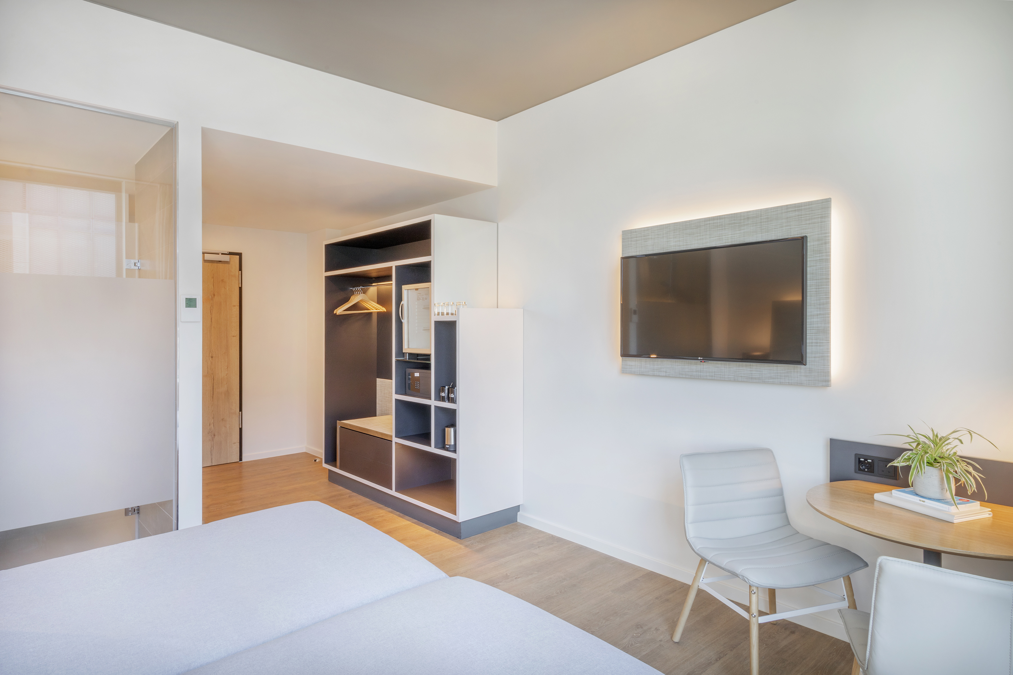 Modern hotel room with bed, wall-mounted TV, small desk, and open closet.