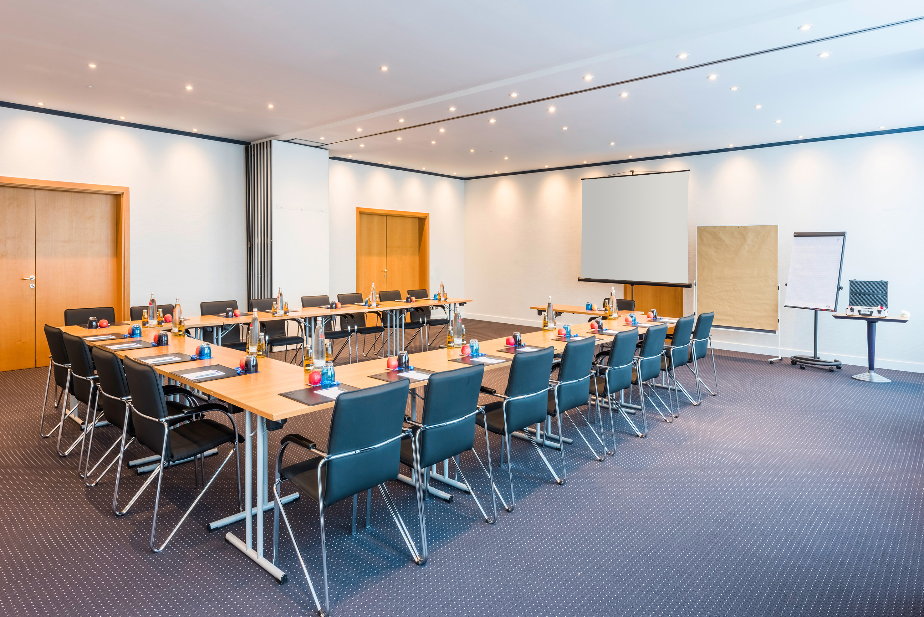 U-shape conference room with projector screen, tables, chairs for meetings.
