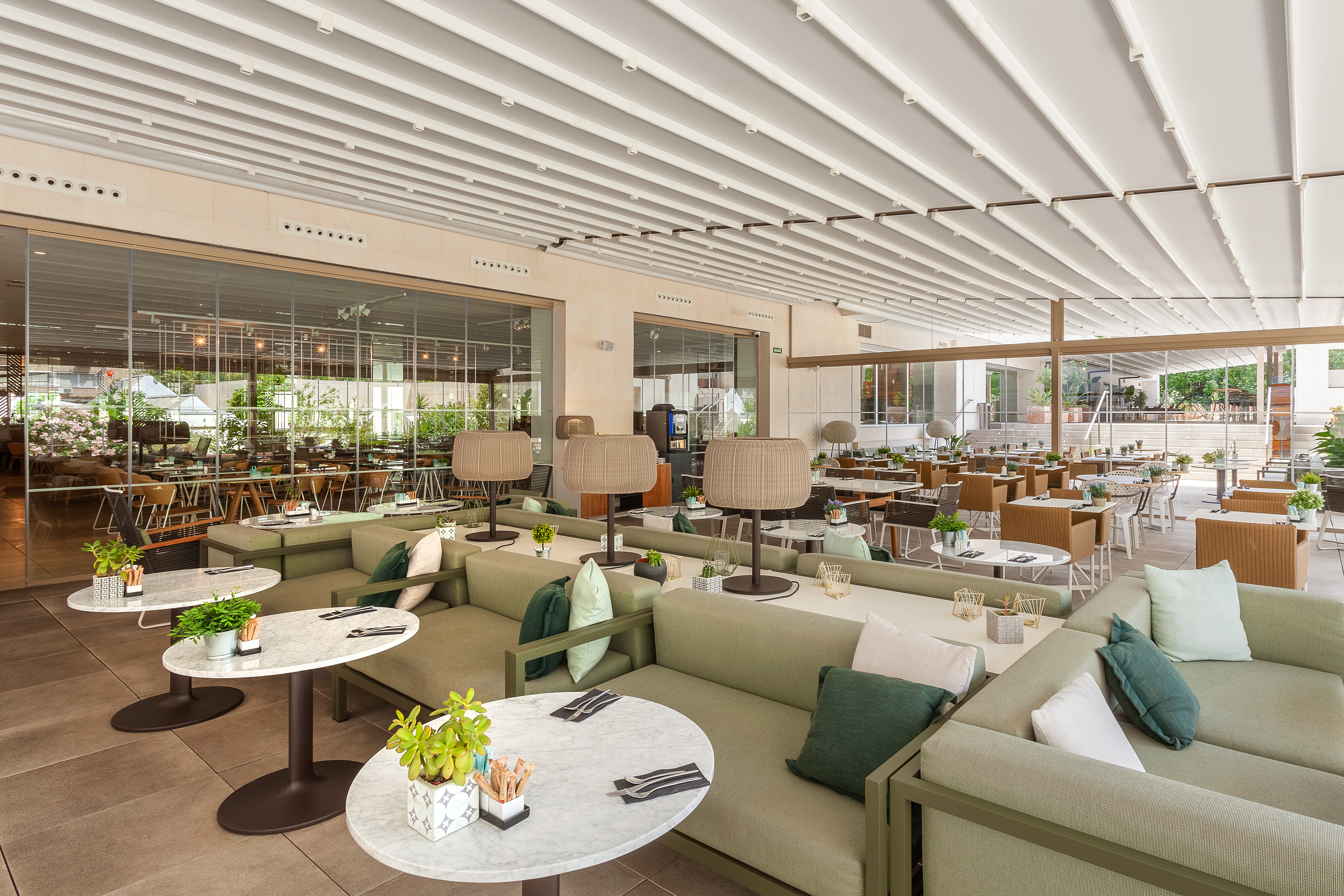 Spacious restaurant terrace with green lounge seating, marble tables, and retractable roof.