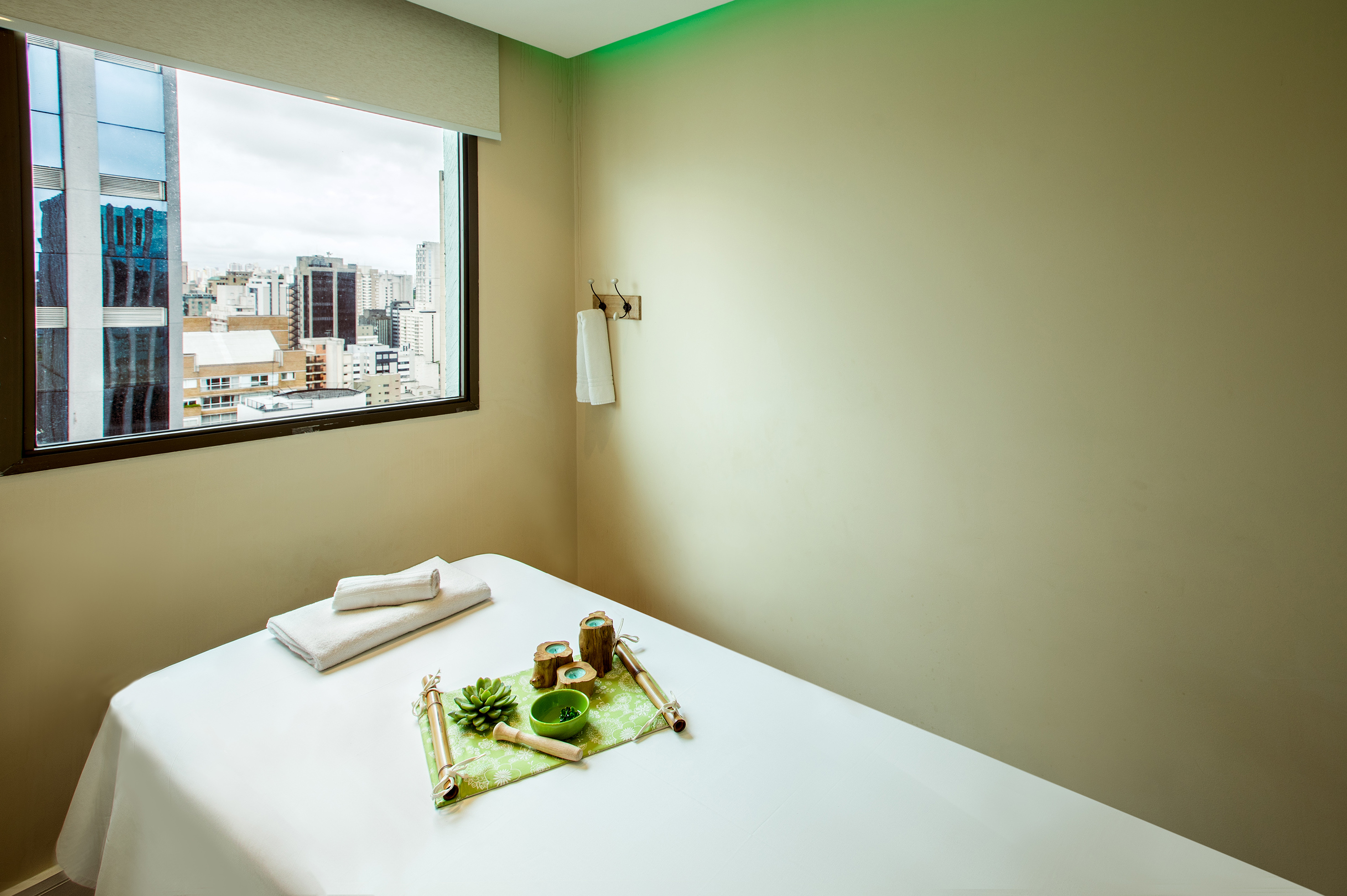 Spa treatment room with city skyline view, white massage bed, and zen decor.