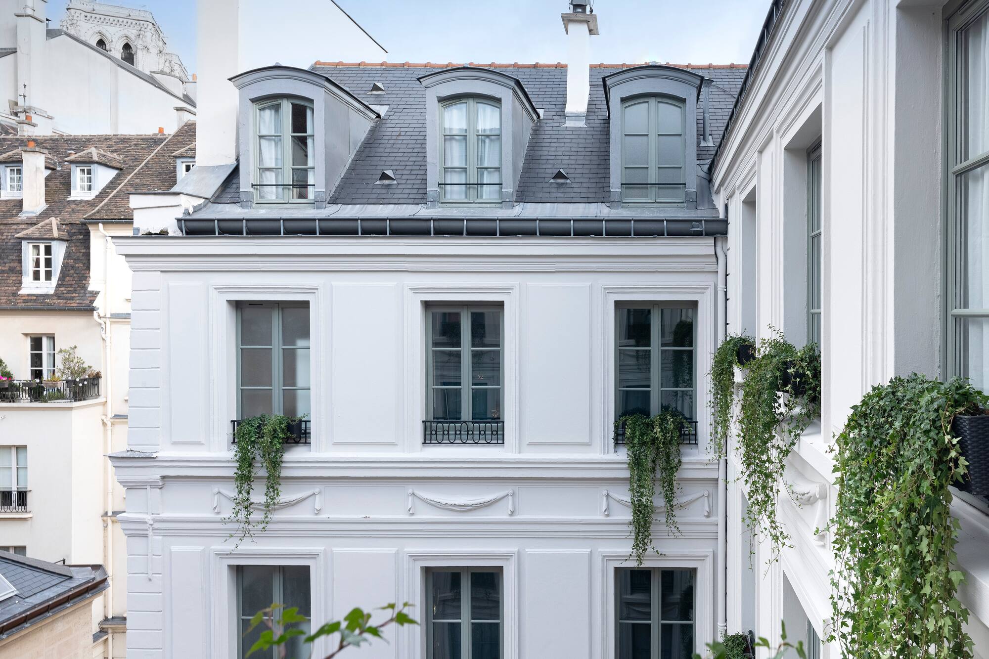 White Parisian building with grey dormer windows, slate roof, and lush ivy.