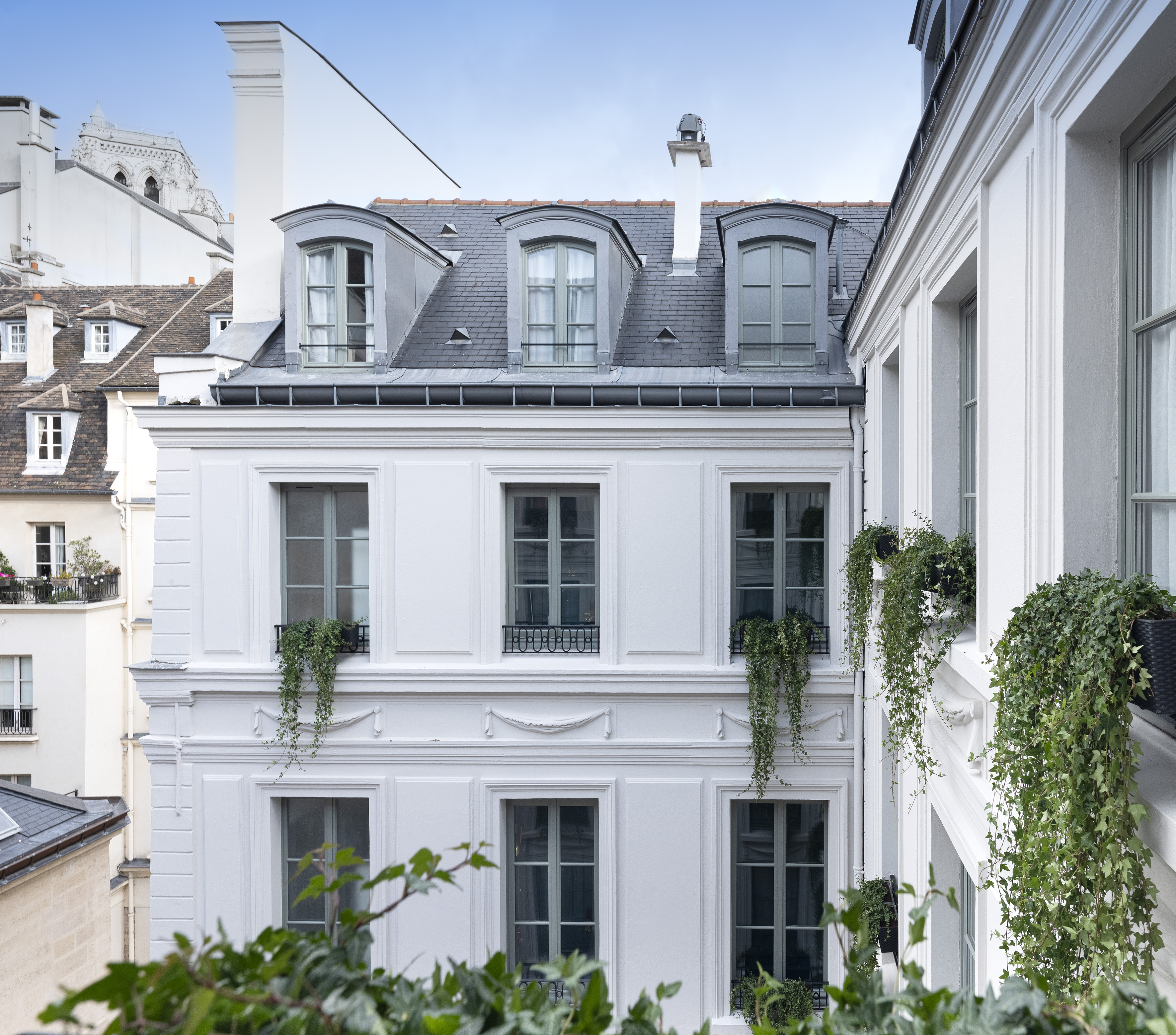 White Parisian building with grey dormer windows, slate roof, and lush ivy.