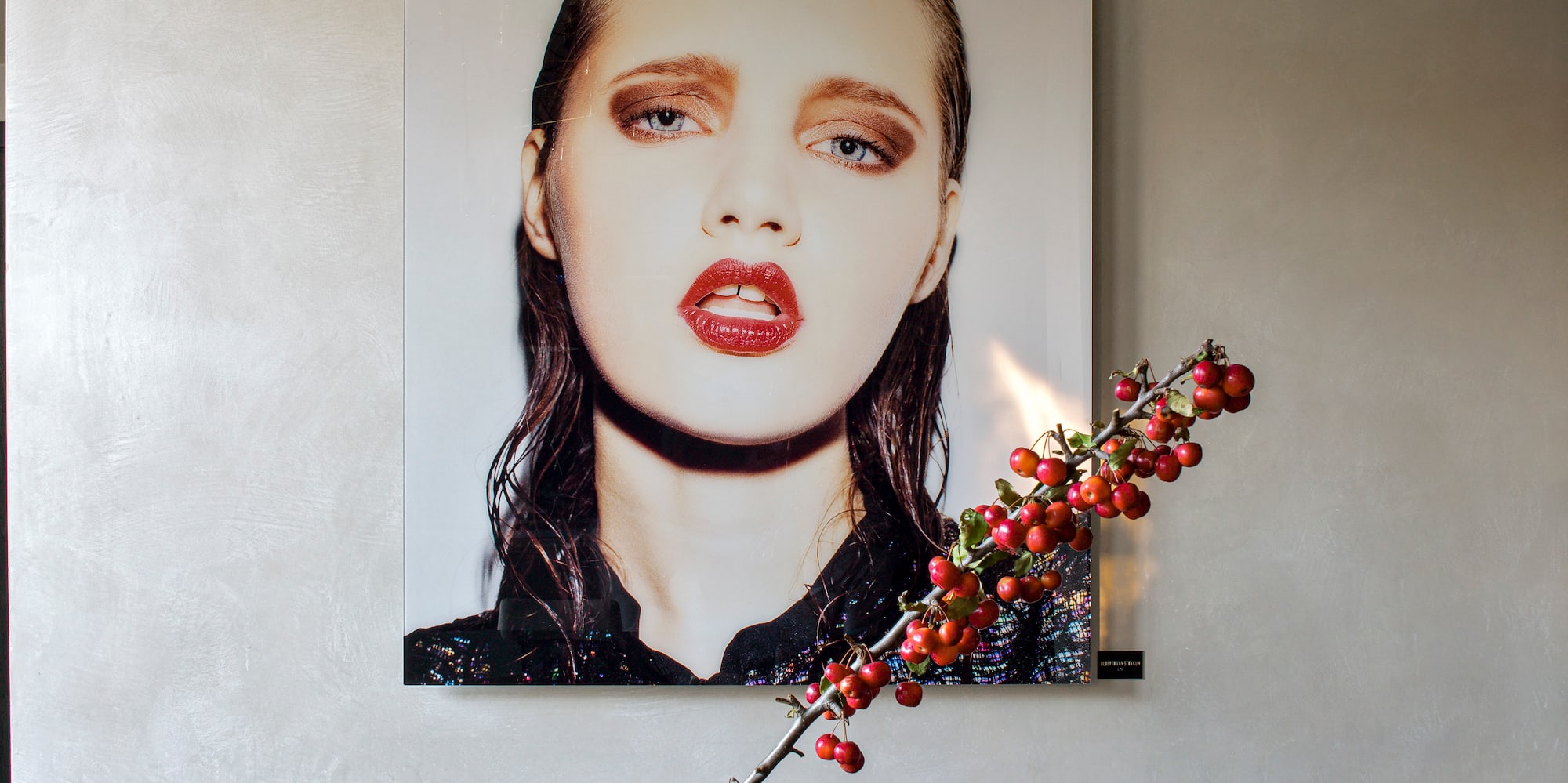 Dining room with modern portrait art, brass chandelier, and berries in grey vase.