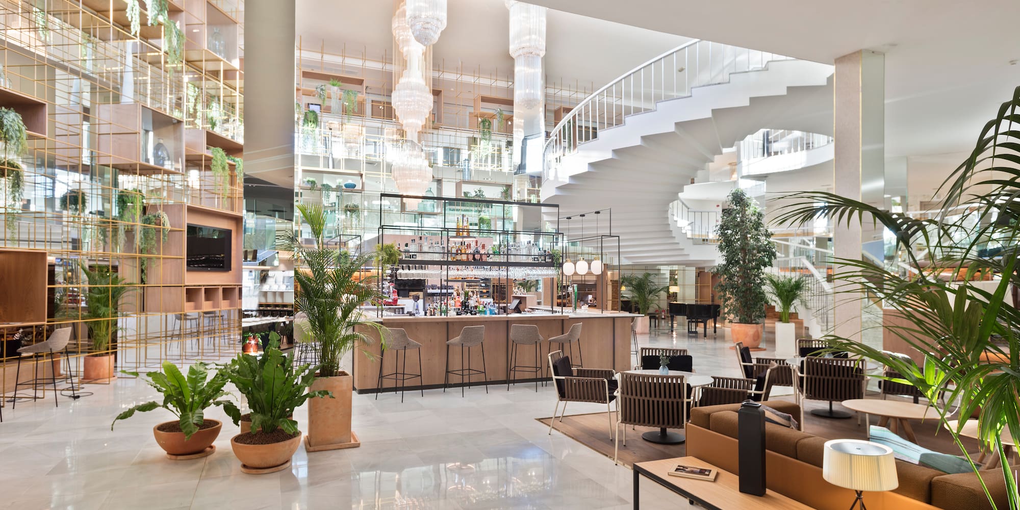 Modern hotel lobby with bar, lounge, spiral staircase, and indoor plants.