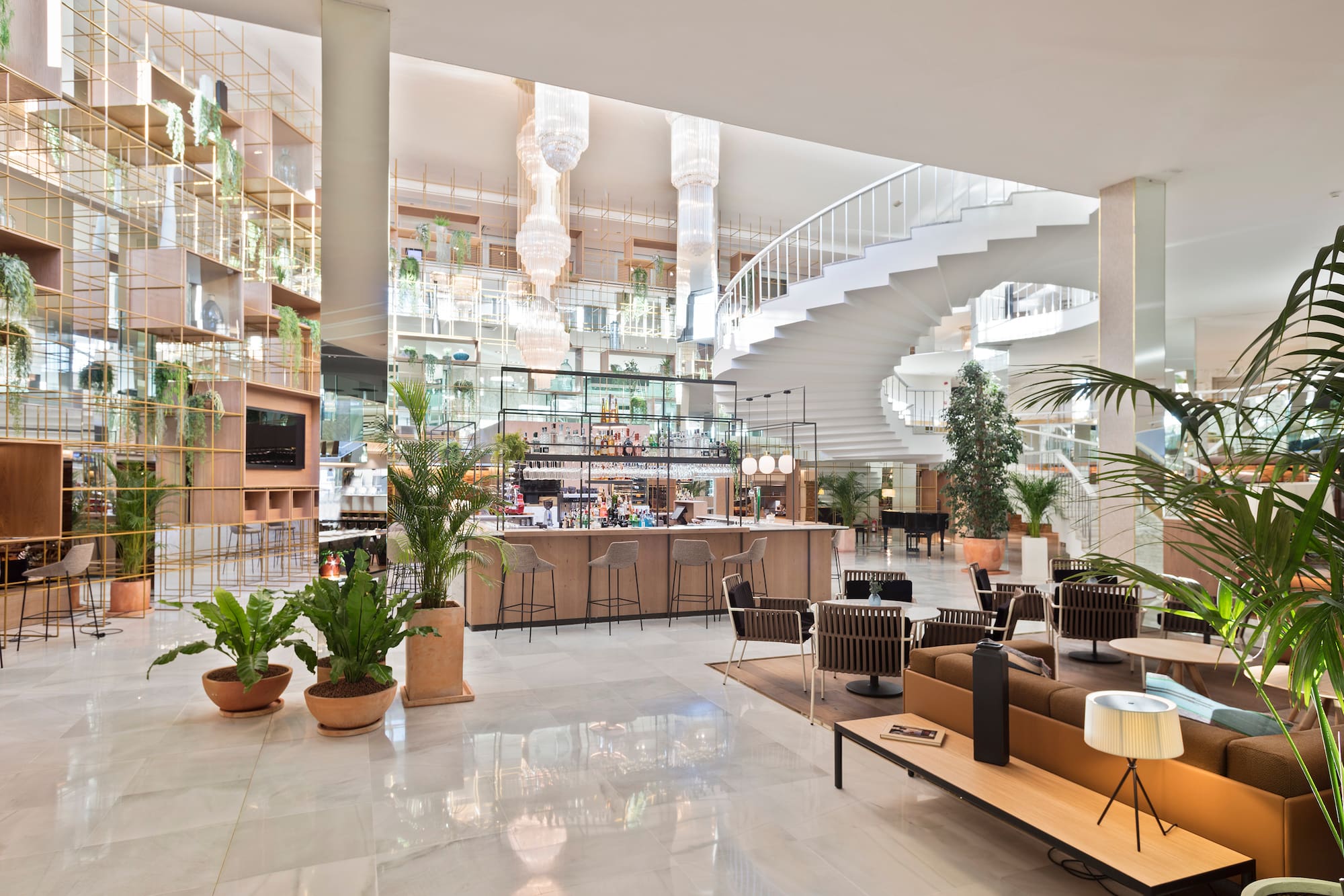 Modern hotel lobby with bar, lounge, spiral staircase, and indoor plants.