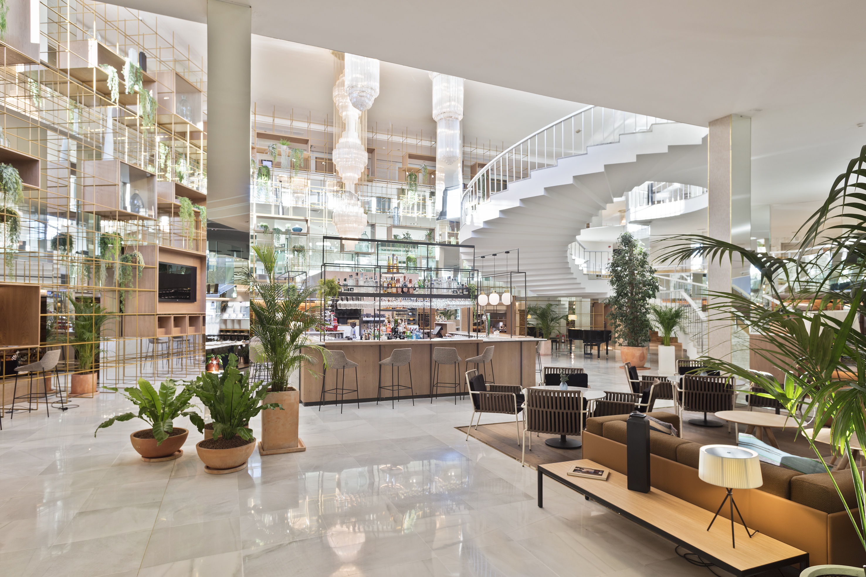 Modern hotel lobby with bar, lounge, spiral staircase, and indoor plants.