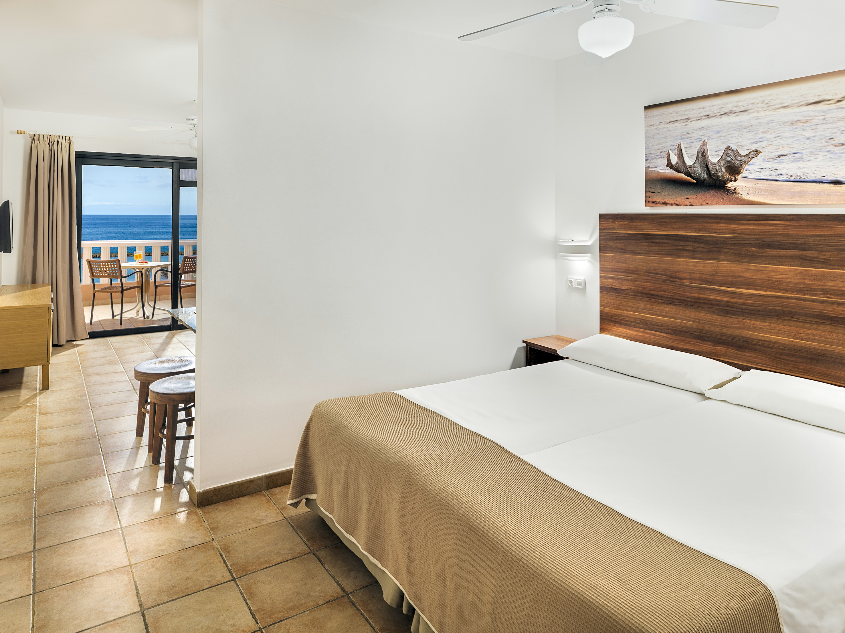 Hotel room with ocean view balcony, double bed, and tiled floor.