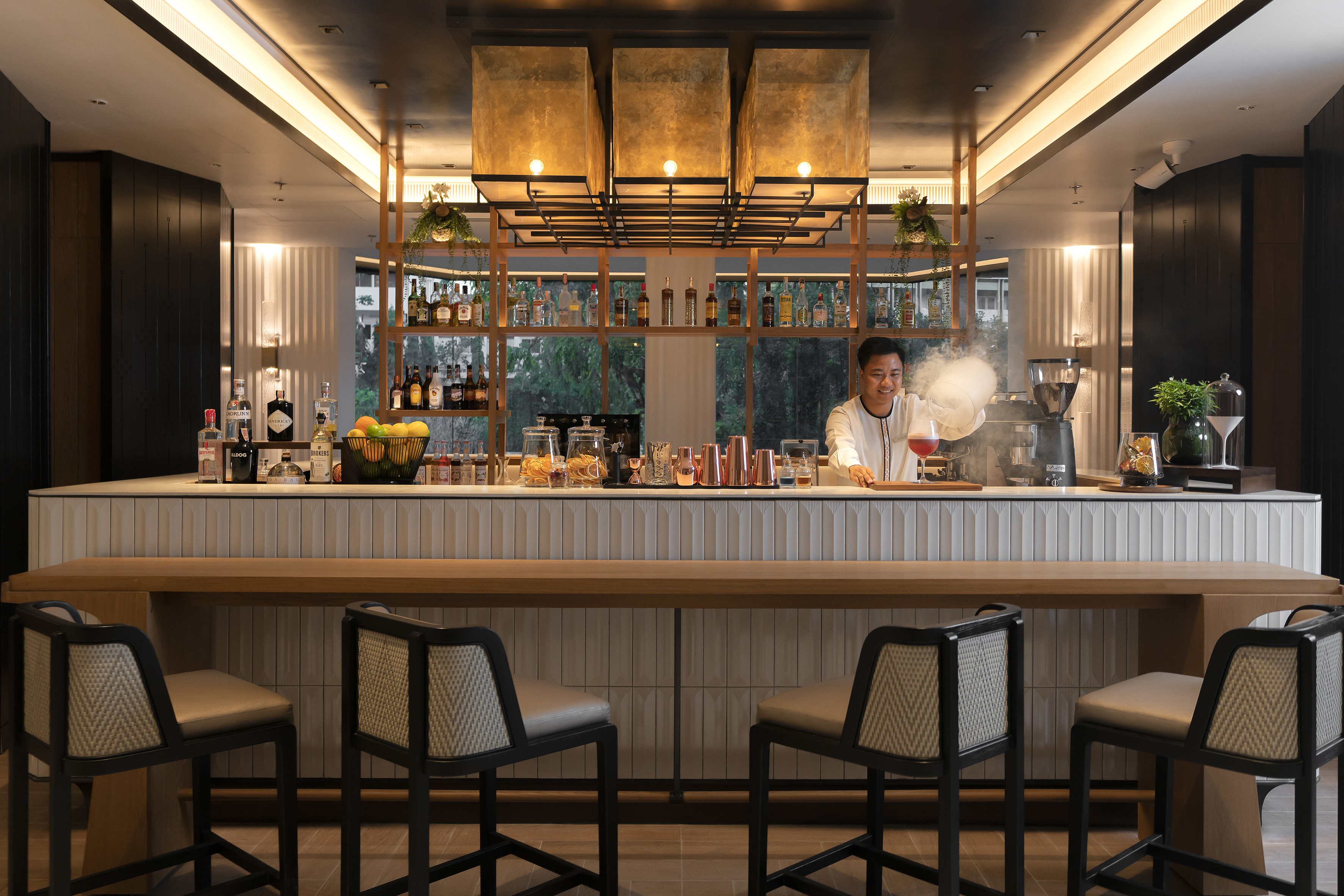 Smiling bartender making a smoky cocktail at a modern bar with liquor bottles.