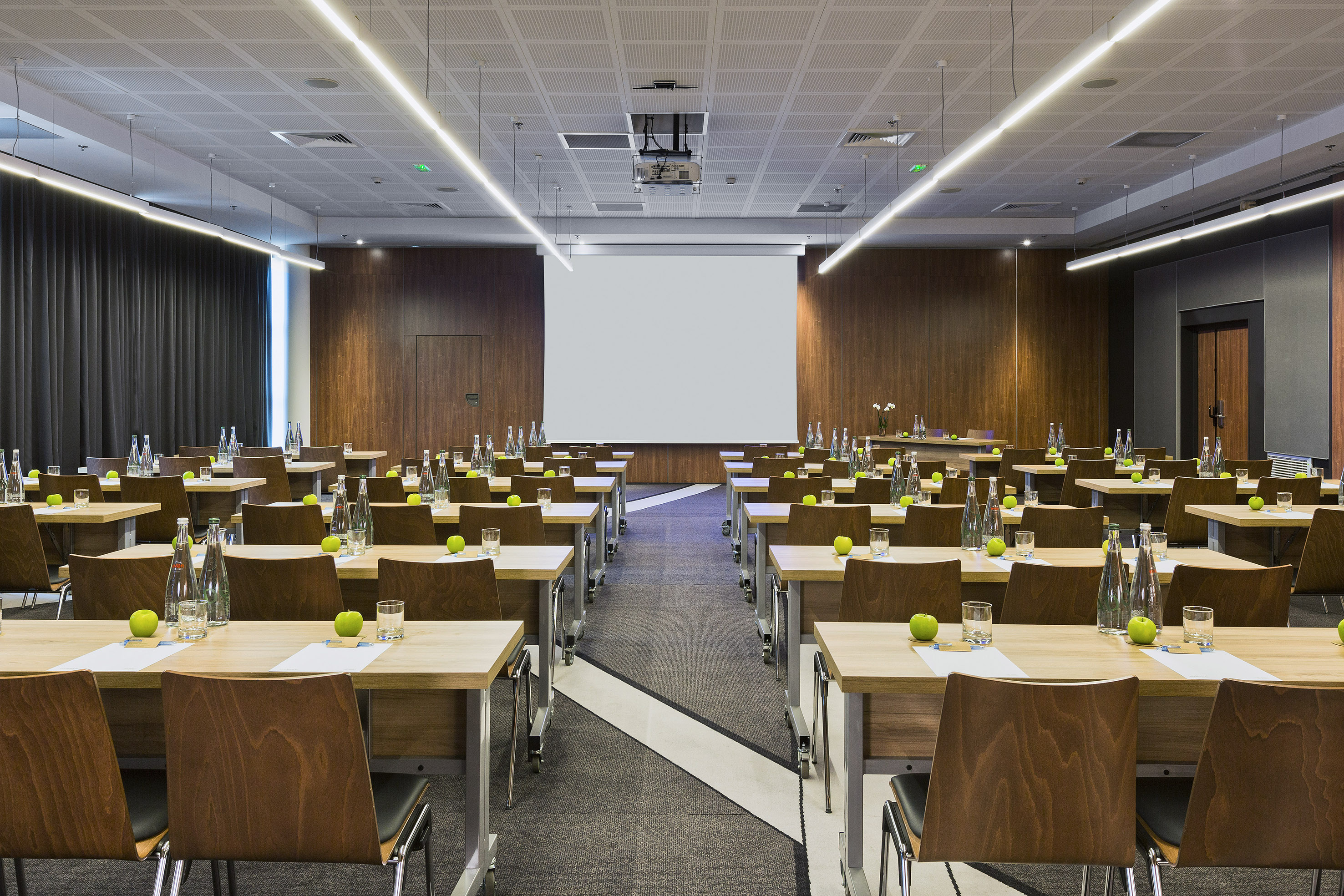 Modern conference room with tables, chairs, projector screen, and amenities.