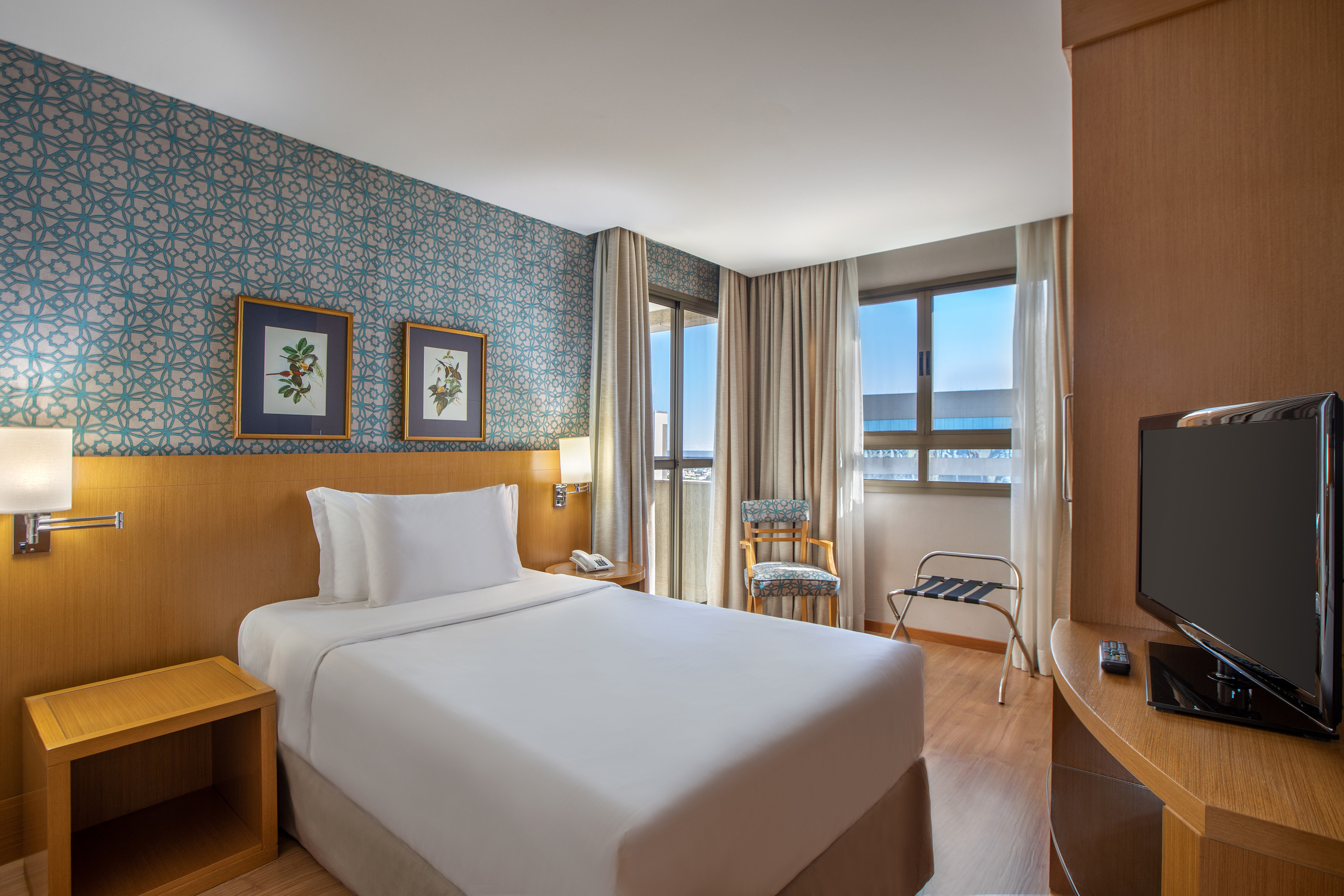 Modern hotel room with single bed, patterned teal wallpaper, and large windows.