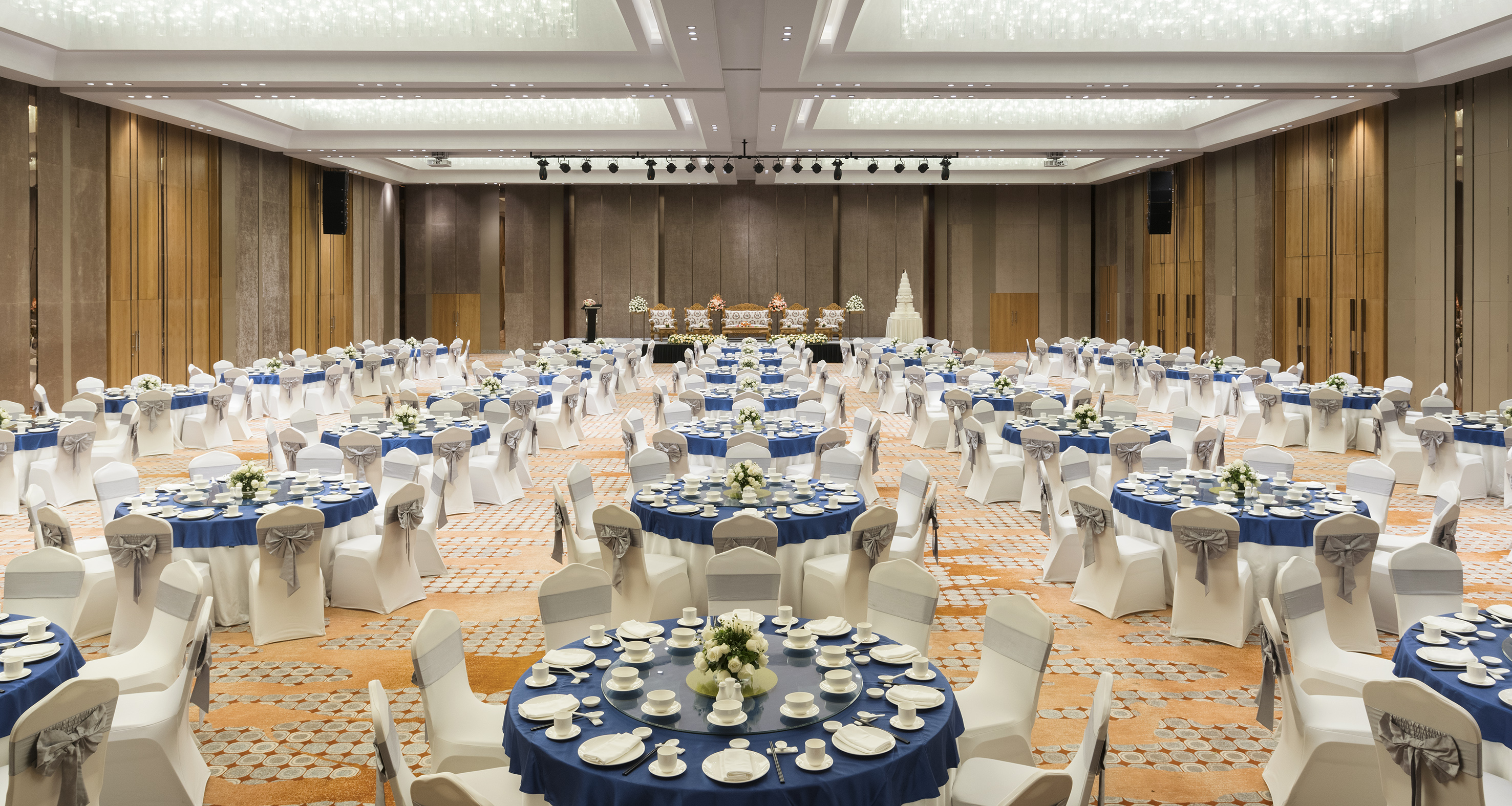 Spacious ballroom set for banquet, blue and white dining tables, white chairs.