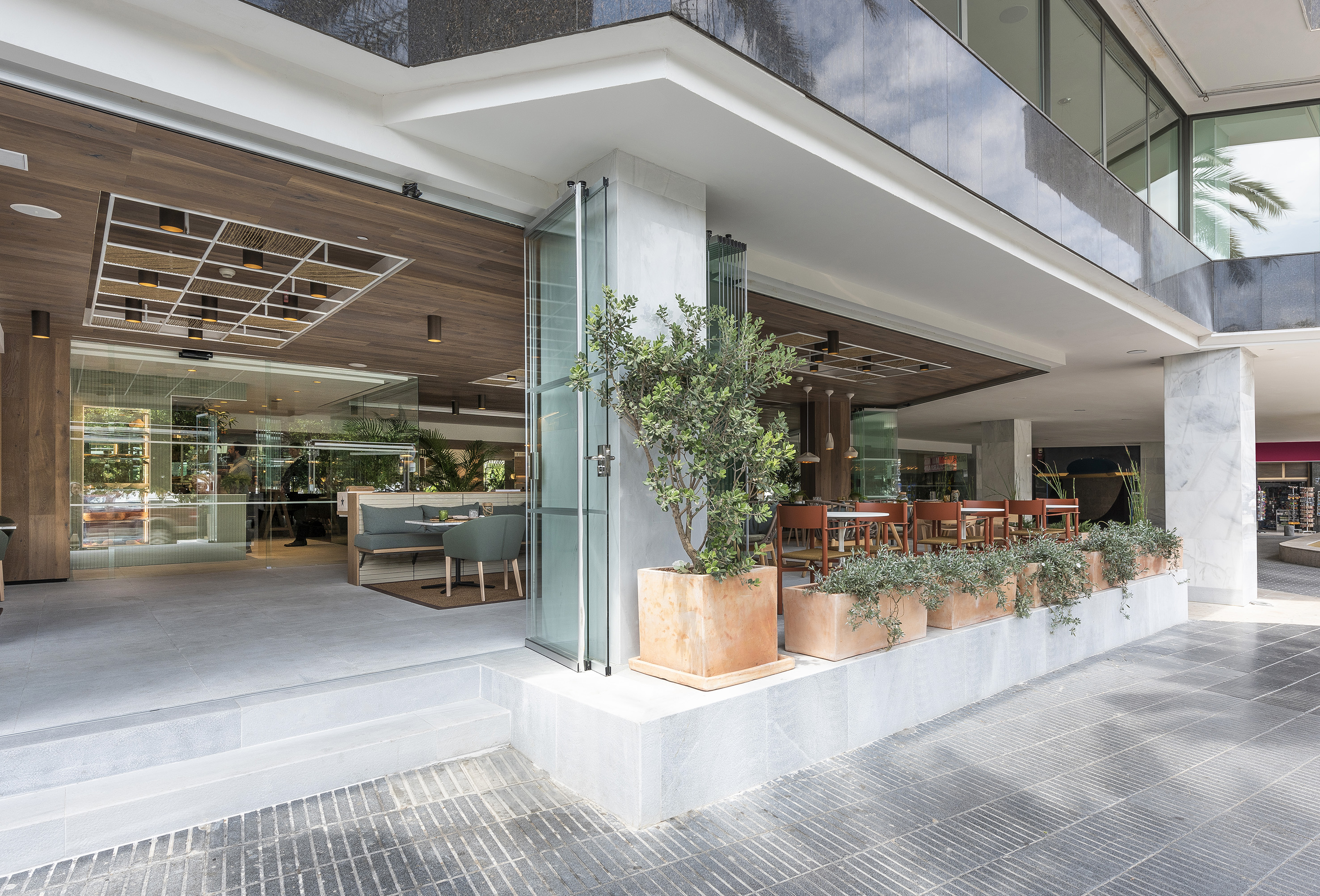 Modern restaurant exterior with outdoor dining area, wooden ceiling, and planters.