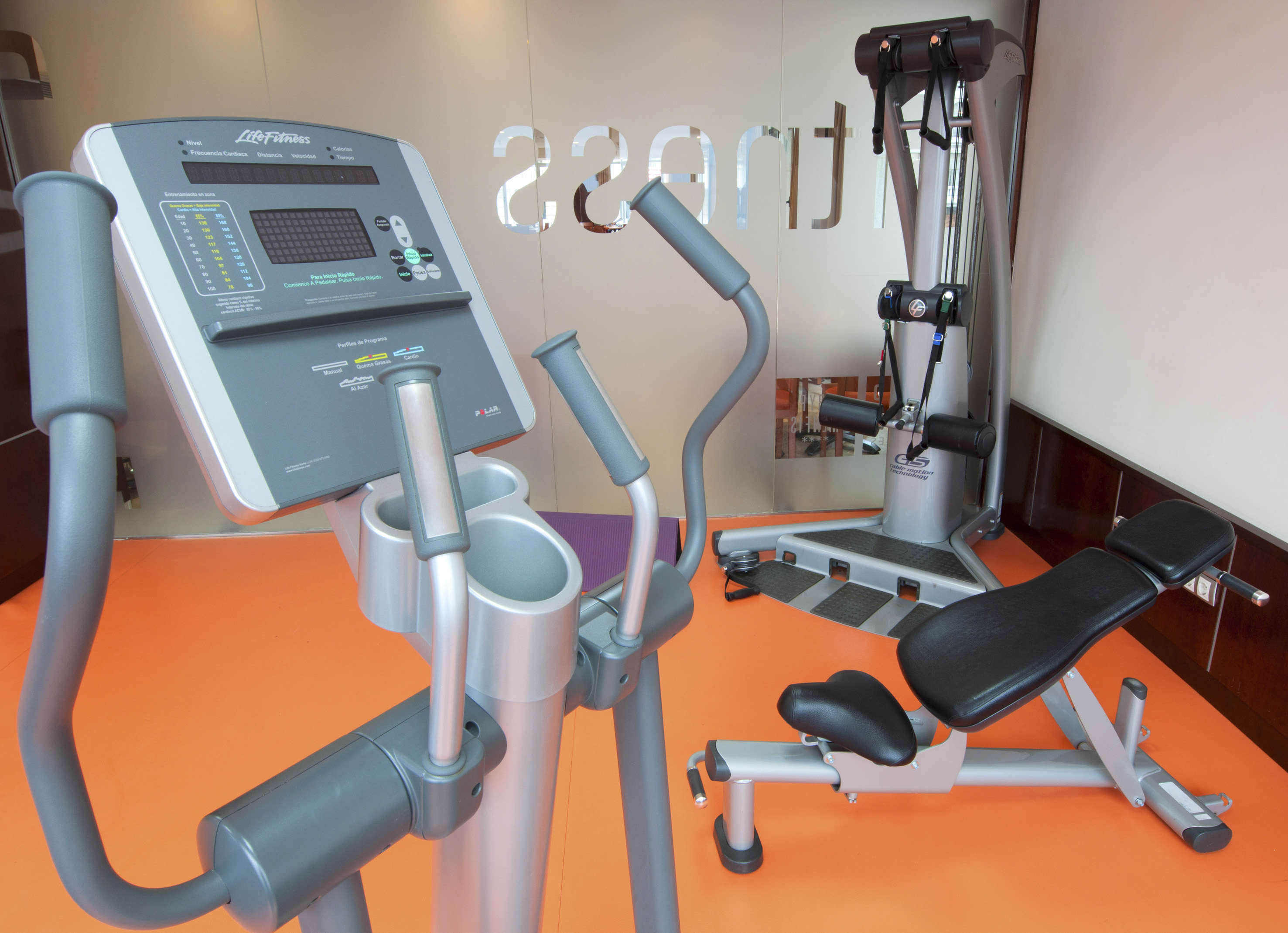 Modern gym with Life Fitness elliptical, cable machine, and workout bench.
