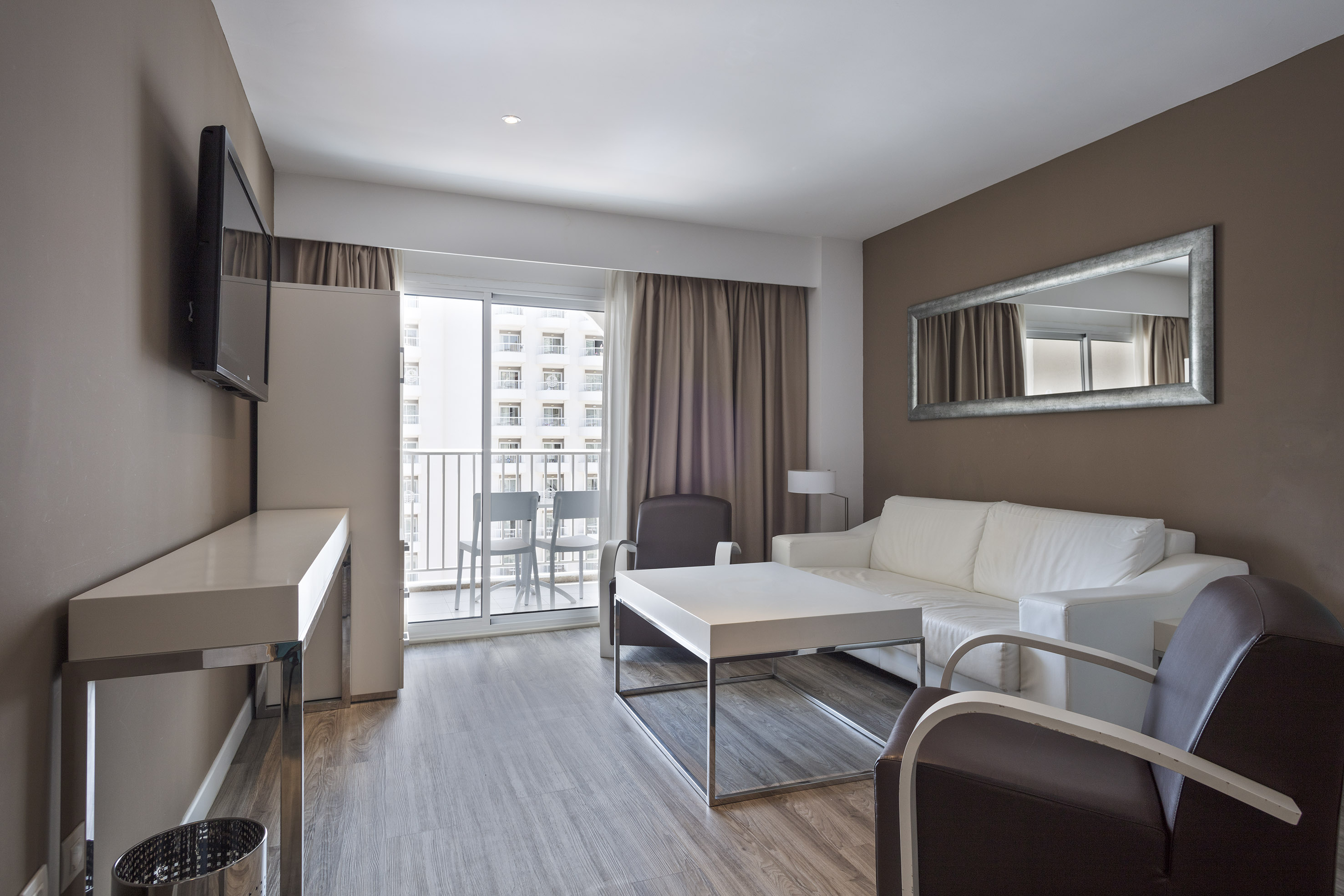 Modern hotel suite living room, white sofa, armchairs, balcony, TV.